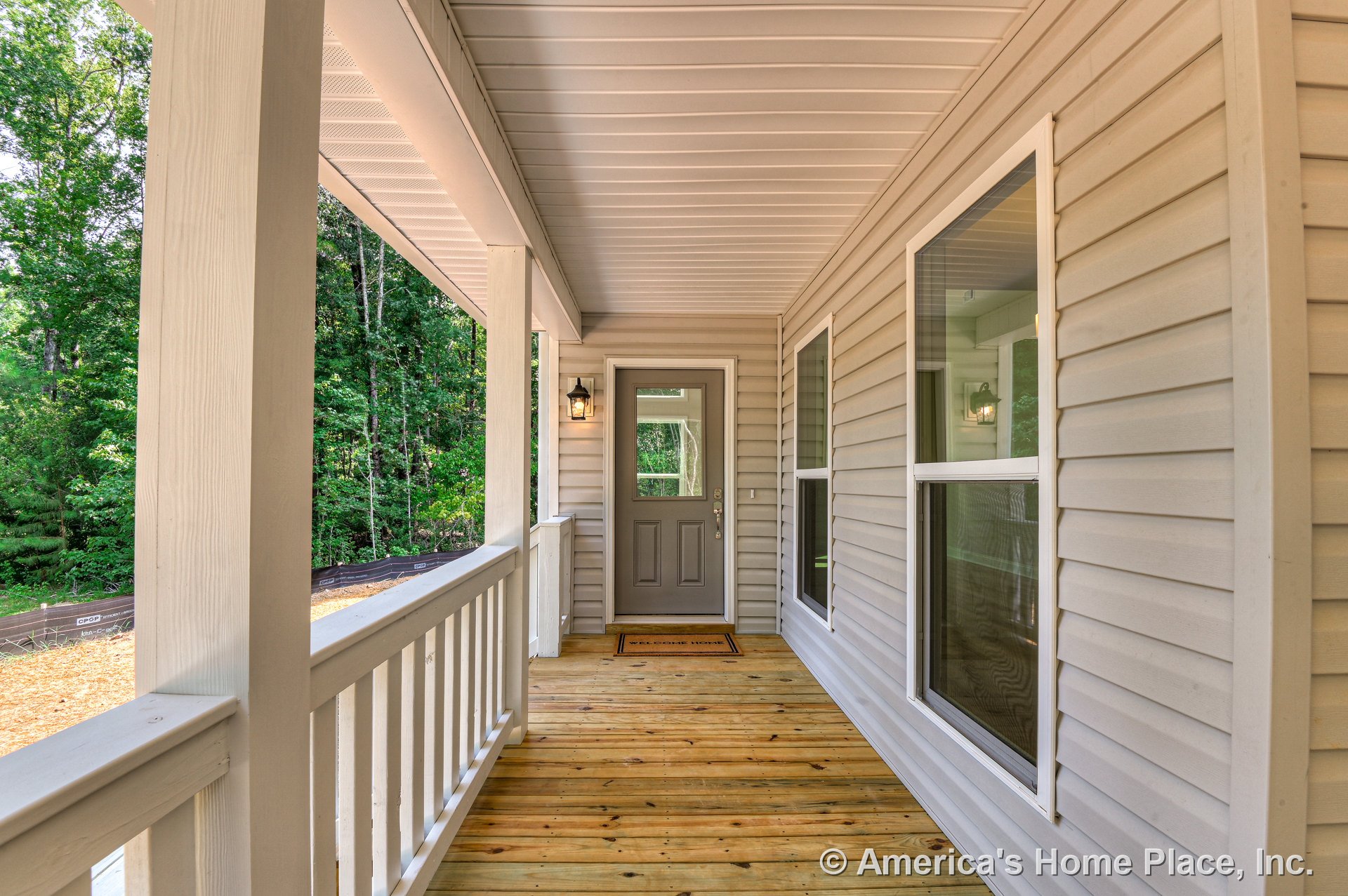 Covered front porch with wood plank flooring, vinyl siding exterior, double-pane windows, entry door, built-in porch light, railing, and trim.