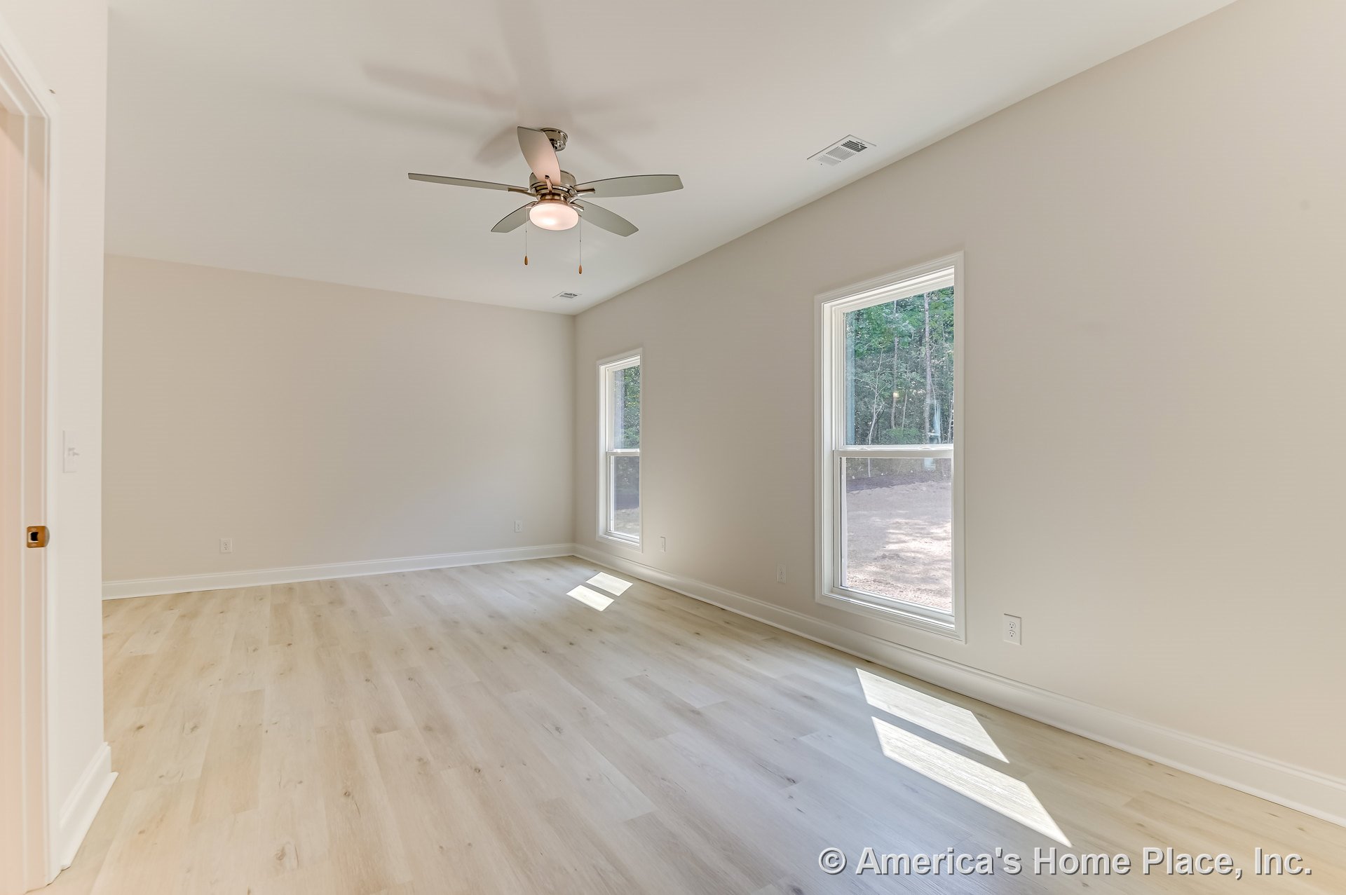 Bright bedroom with light wood plank flooring, two large double-hung windows, neutral painted walls, modern ceiling fan with integrated light, white baseboard trim, and flat