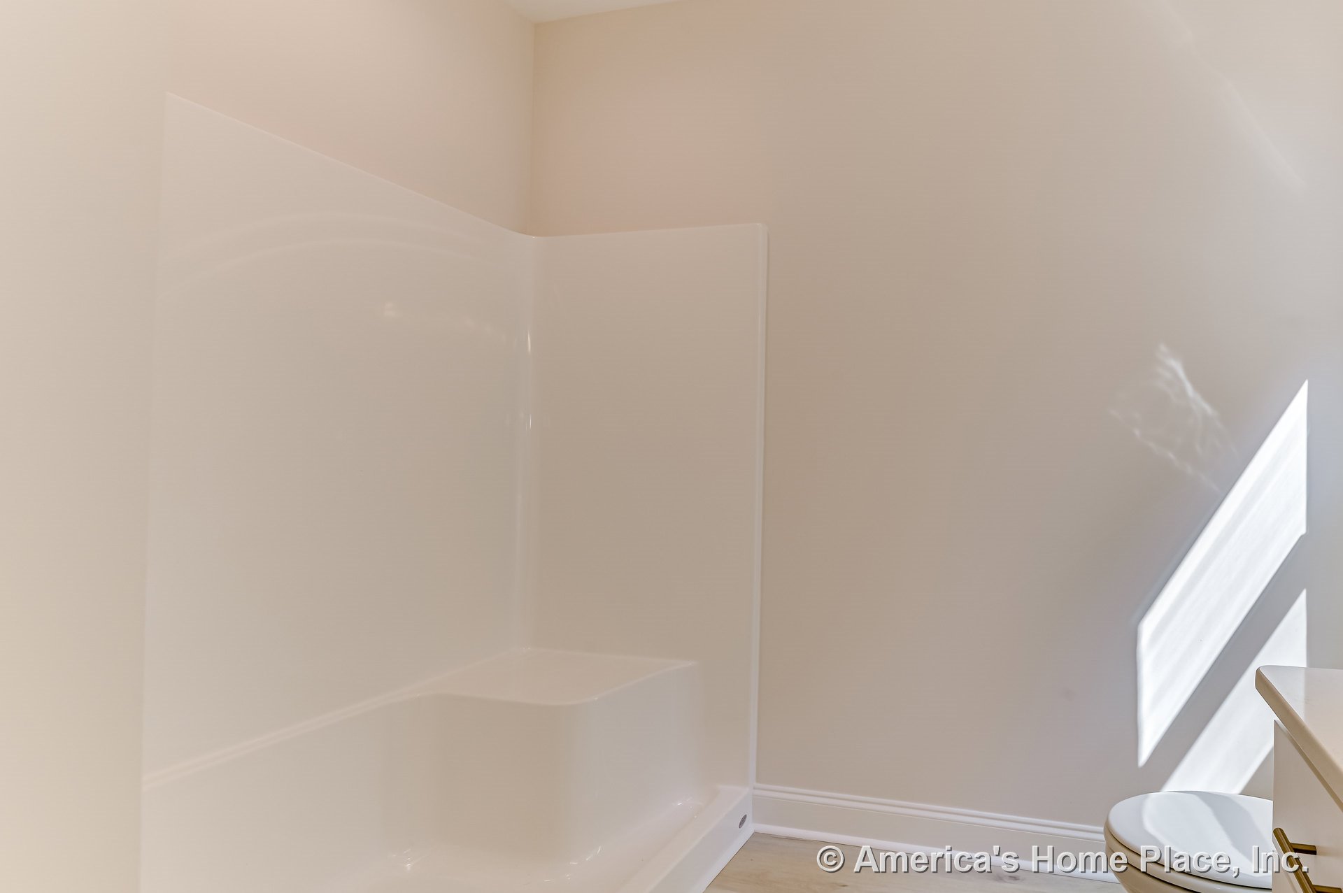 Fiberglass shower enclosure with integrated seat, light beige walls, white baseboard trim, vinyl plank flooring, and partial view of toilet.