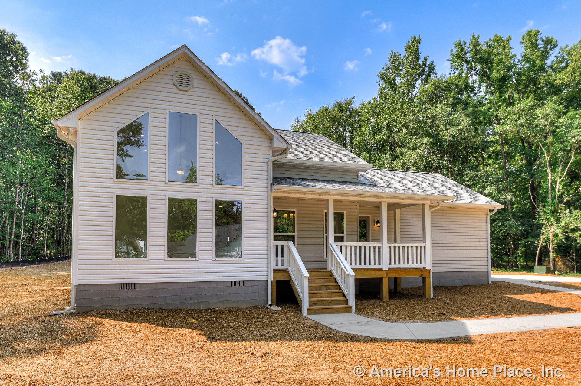 Covered front porch with white railings and steps, multiple tall vertical windows, vinyl siding exterior, gable roof with shingles, exterior lighting fixtures, and detailed trim