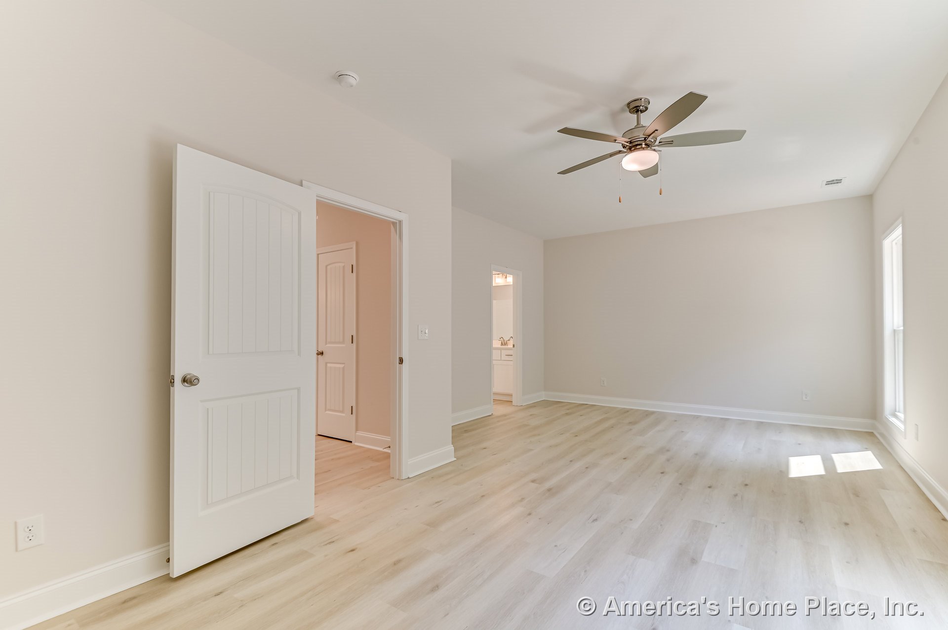 Spacious bedroom with light wood plank flooring, ceiling fan with integrated light, large window for natural light, white paneled interior doors, neutral wall paint, and wide