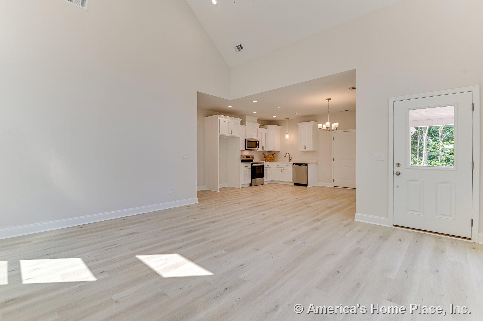 Open-concept living area with vaulted ceiling, light wood flooring, recessed lighting, modern kitchen featuring white shaker cabinets, stainless steel appliances, pendant and