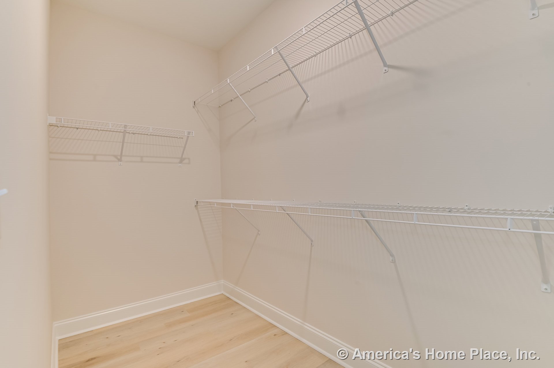 Walk-in closet with built-in white wire shelving, light wood flooring, beige walls, and baseboard trim, showcasing open storage space and permanent fixtures.