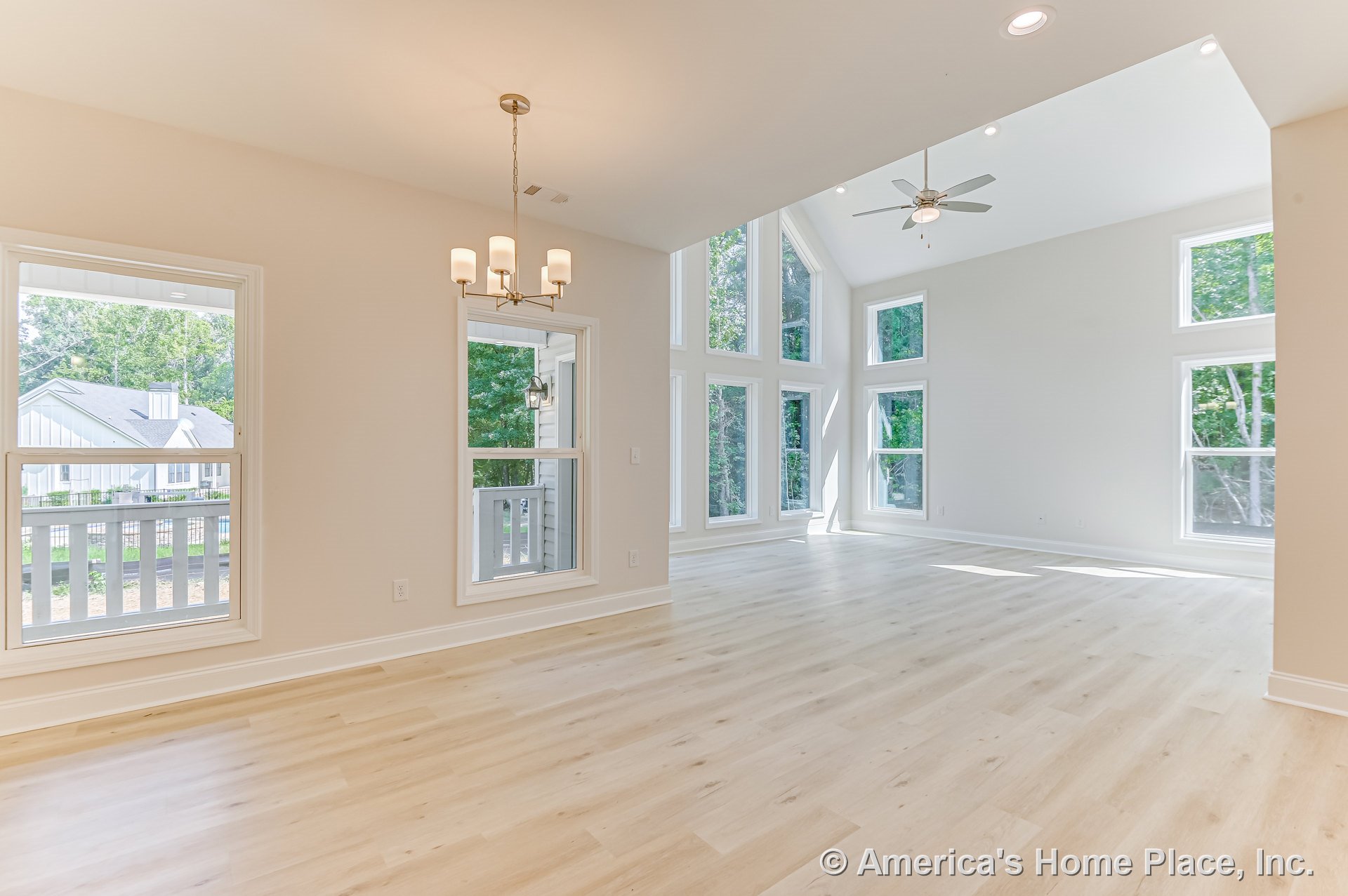 Open living and dining area with vaulted ceiling, recessed lighting, ceiling fan, multiple tall windows, light wood plank flooring, white trim and baseboards, and modern chandelier