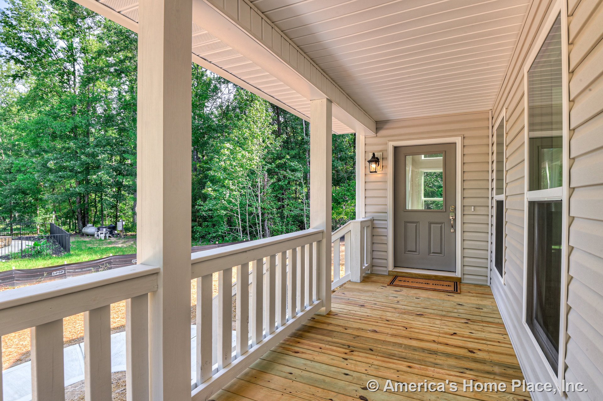 Covered front porch with wood plank flooring, white vertical railing, gray entry door featuring a glass window, wall-mounted porch light, double-pane windows, and light-colored