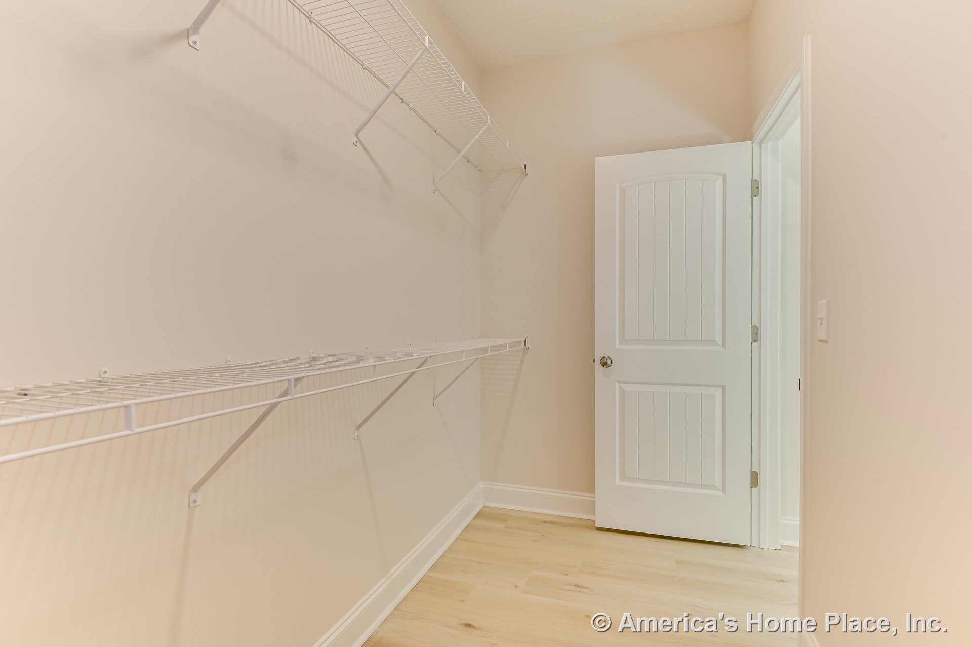 Walk-in closet with wire shelving, light wood flooring, white paneled door, beige walls, baseboard trim, and high ceiling.