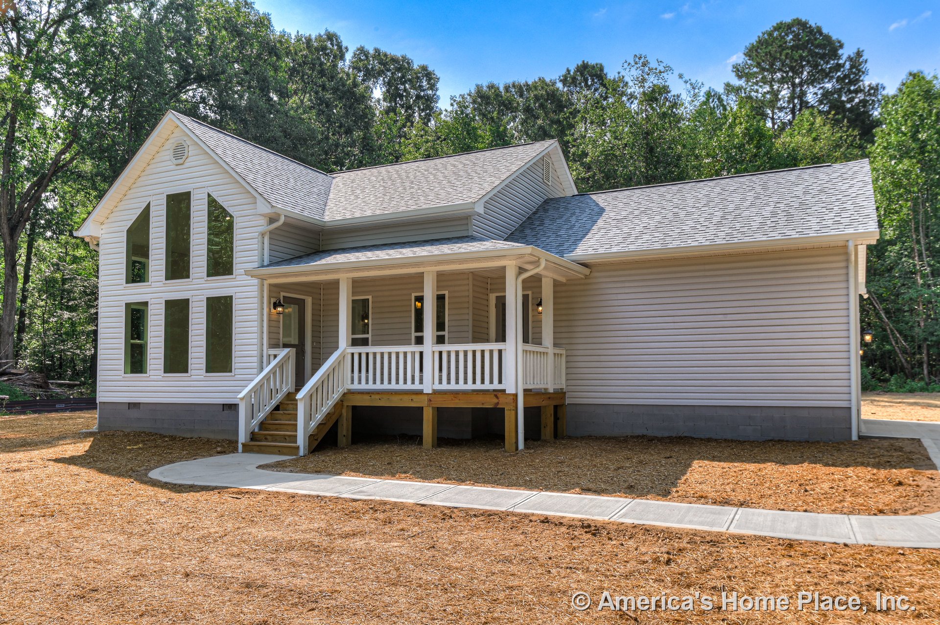 Covered front porch with white railings, large vertical windows on the facade, gray shingle roof, light vinyl siding exterior, concrete walkway leading to entry steps, white