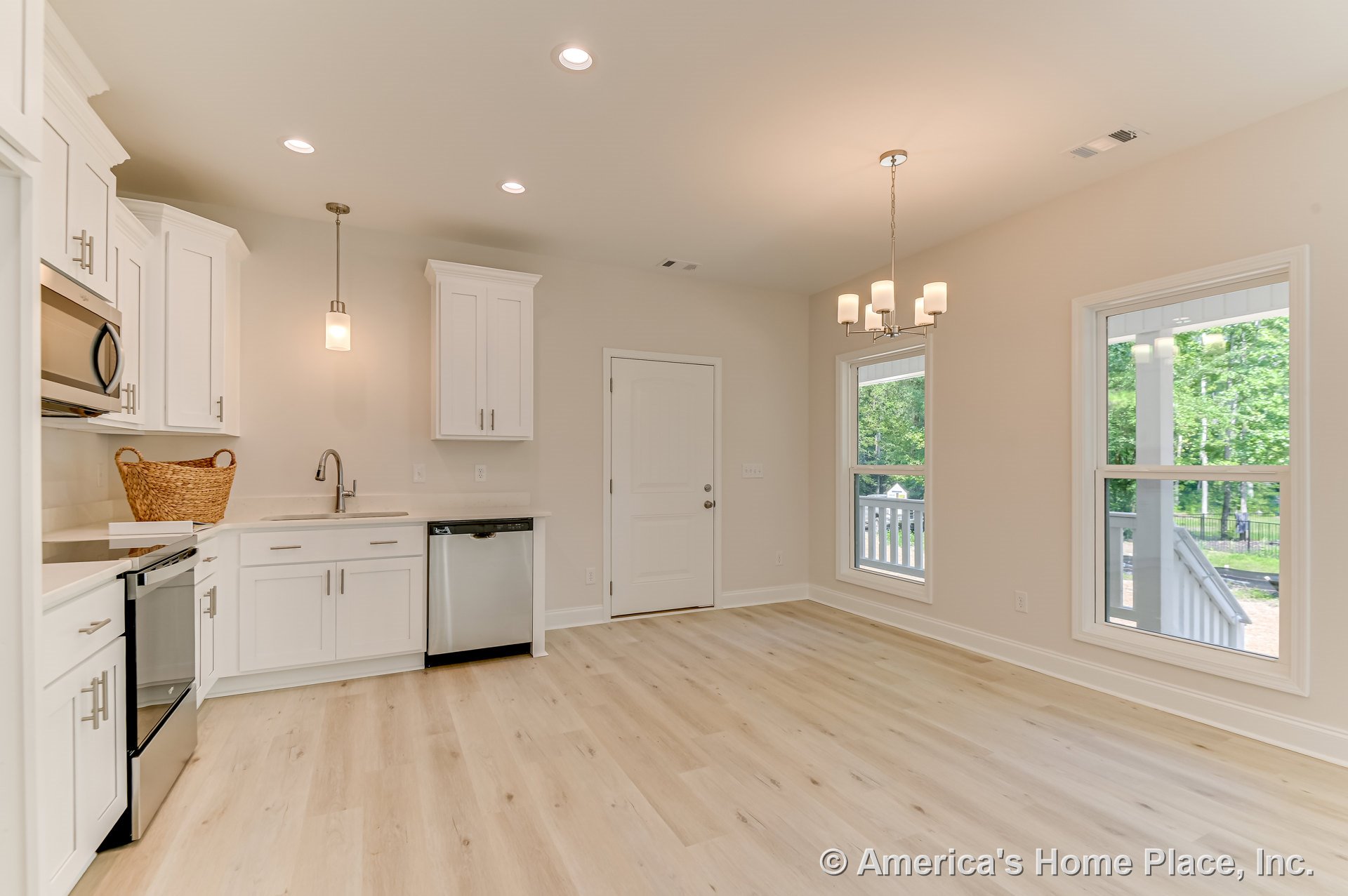 White shaker kitchen cabinets with stainless steel dishwasher and appliances, solid surface countertops, pendant and chandelier lighting, large windows with decorative trim, light