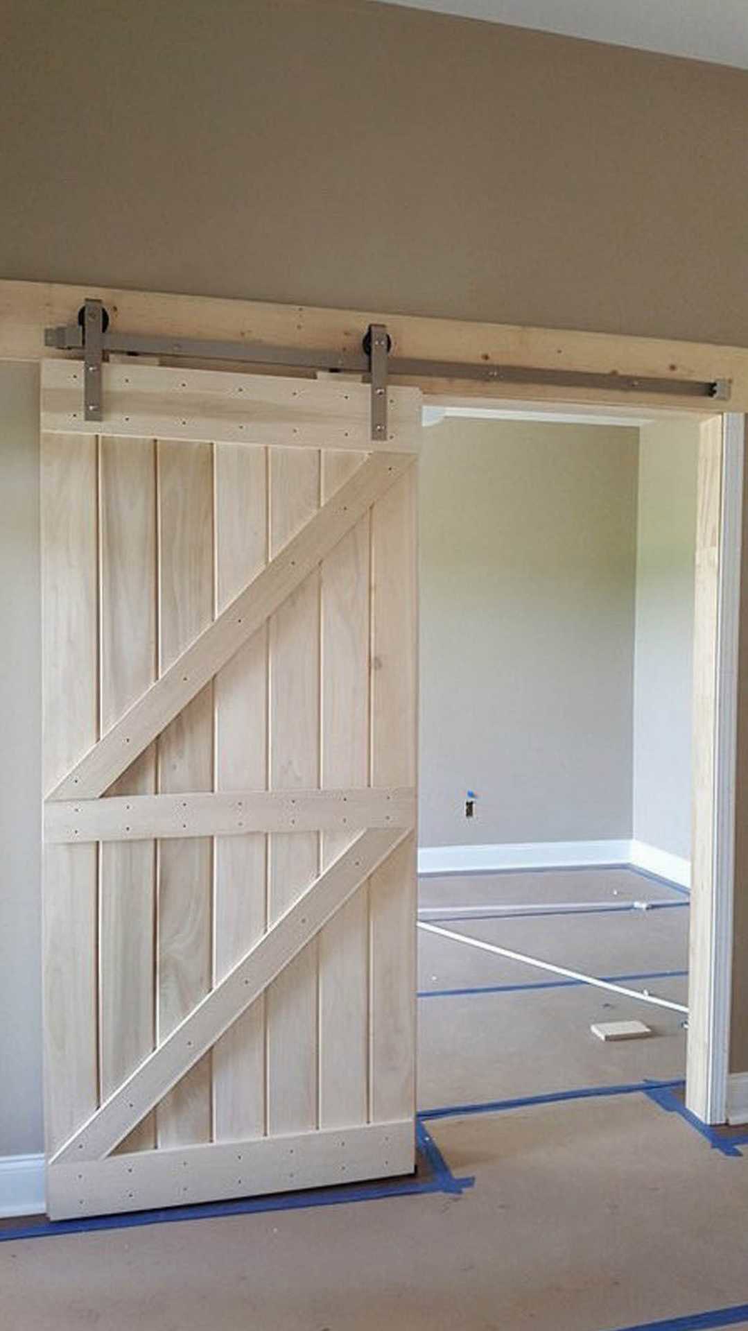 White sliding barn door with crossbuck design, wood floor with blue painter’s tape, white paneled walls, and decorative molding in a residential interior.