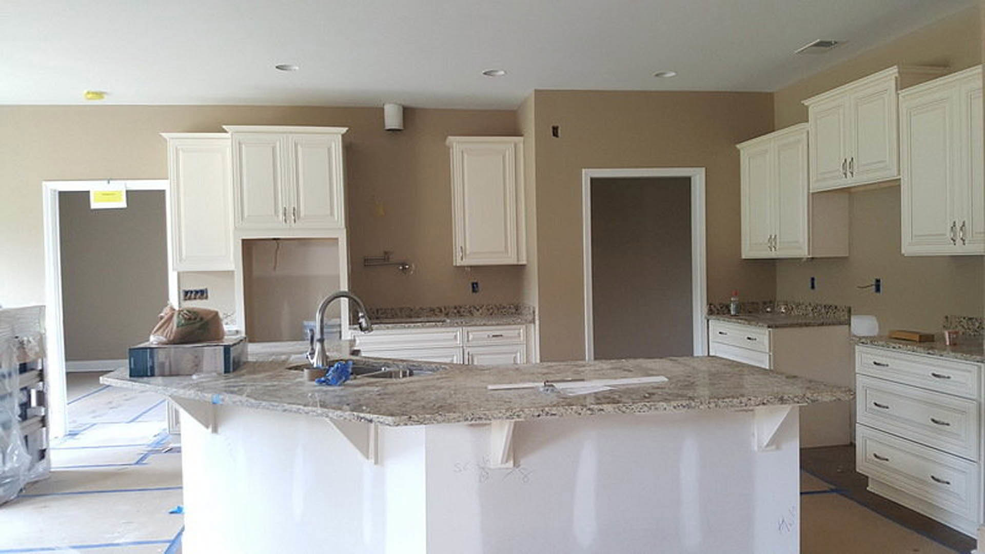 Granite kitchen countertops with white cabinetry, stainless steel handles, white backsplash, and built-in sink; yellow rectangular object with black text on counter, white framed