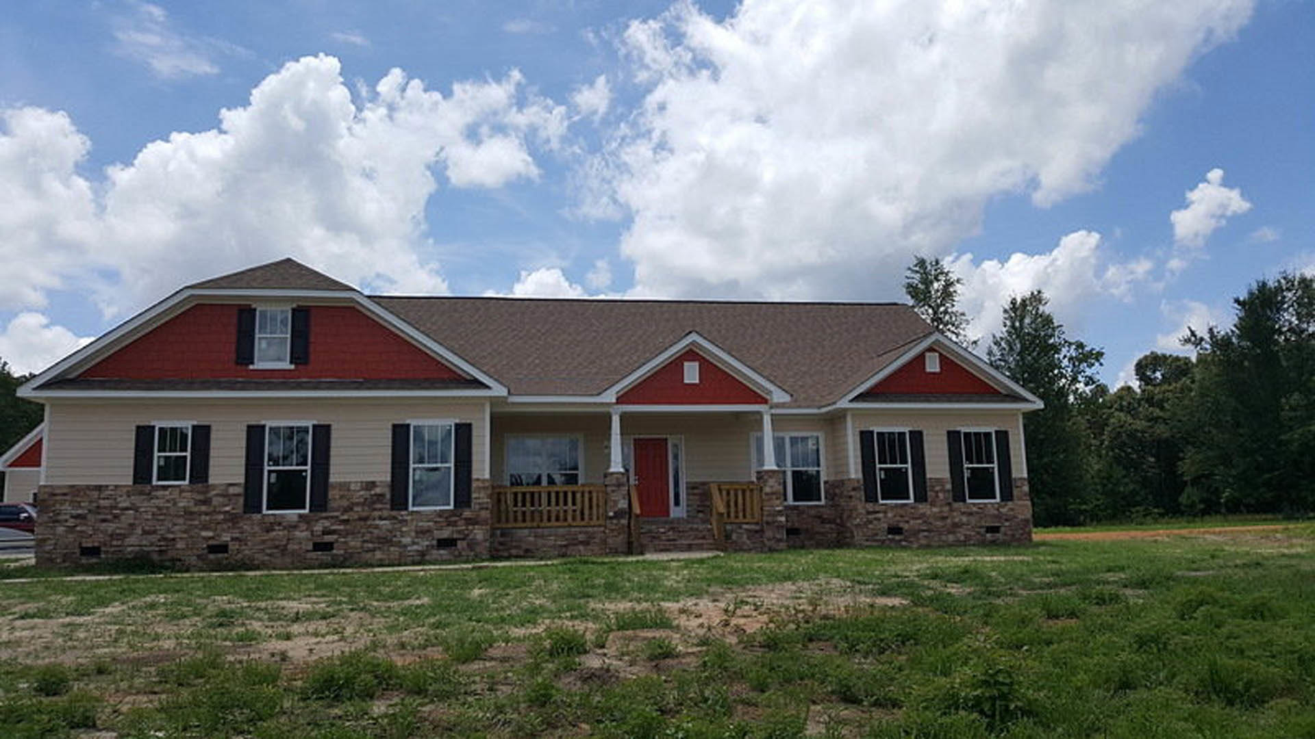 Brick house with two red doors, white-framed windows, green lawn, and blue sky with scattered clouds