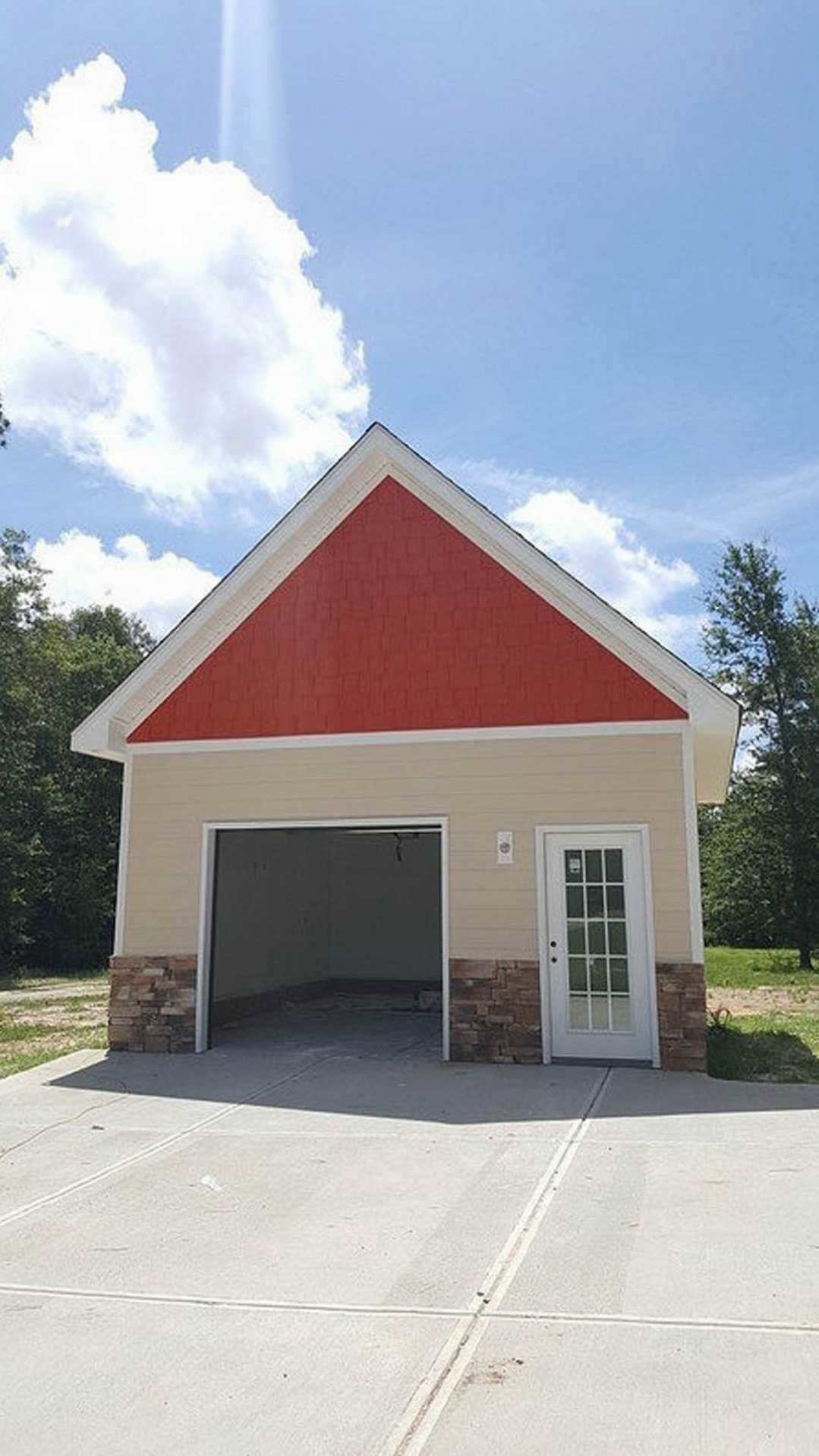 Garage with red roof and white trim, brick wall, white garage door featuring glass panes, surrounded by trees and cloudy sky