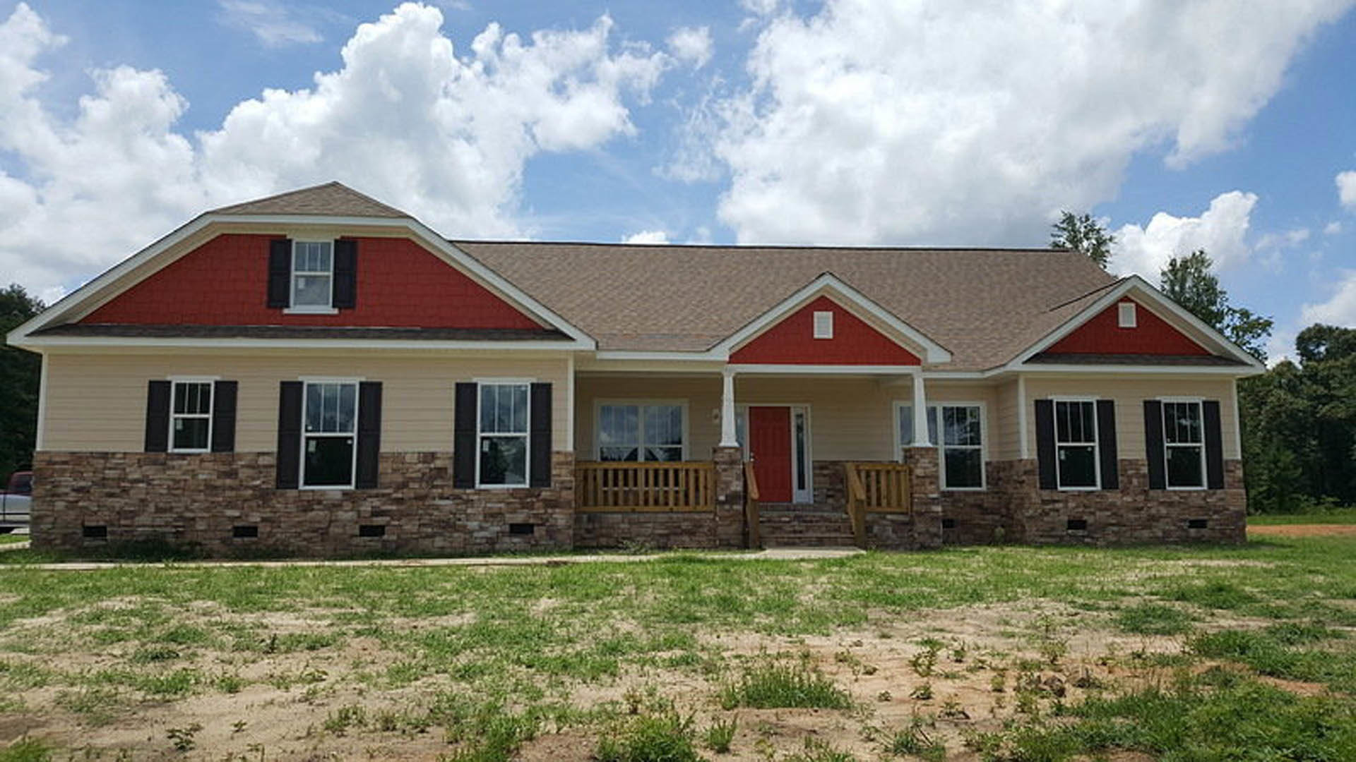 Two-story home with white siding, red front door, covered porch, large windows, manicured grass lawn, and blue sky with scattered clouds