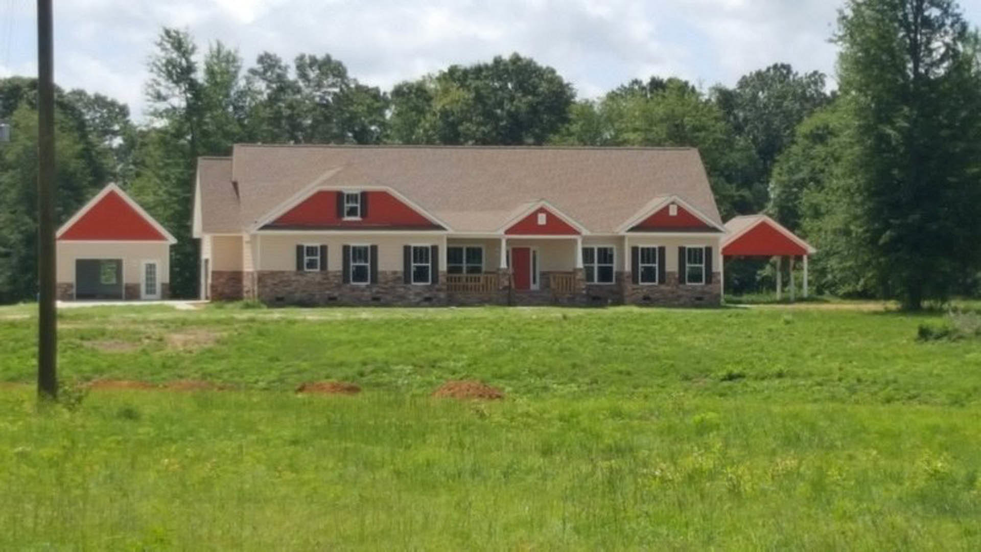 Two-story house with red siding and white trim, white-framed windows, and a green lawn in front, set against a cloudy sky.