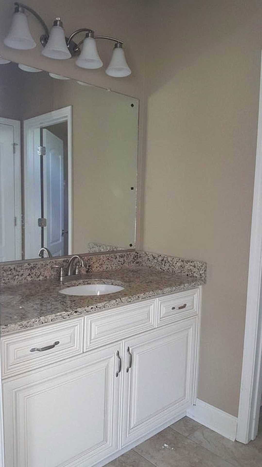 Bathroom with marble countertop, undermount sink, chrome faucet, white cabinetry, wall-mounted mirror, and glass shower door