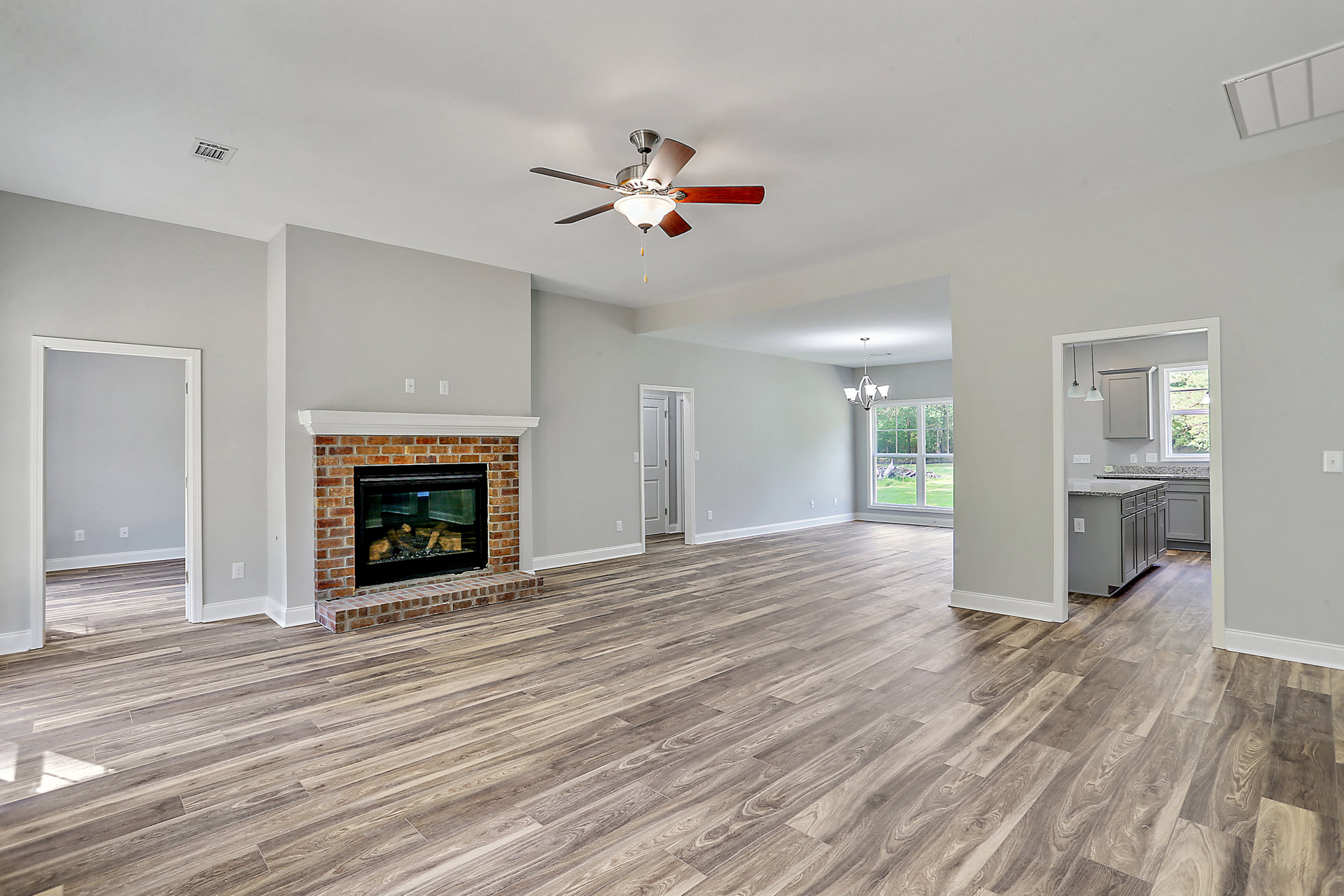 Living room with hardwood flooring, white walls, ceiling fan with light, and fireplace containing stacked wood logs