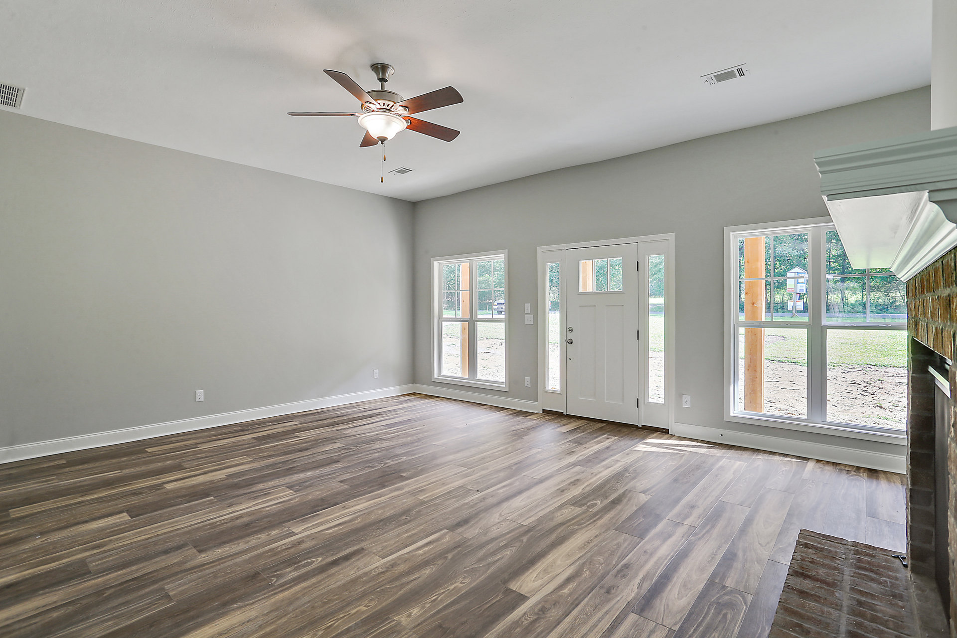 Ceiling fan with light fixture, wood laminate flooring, white door with glass panes, large windows showing parked car outside, neutral walls and ceiling
