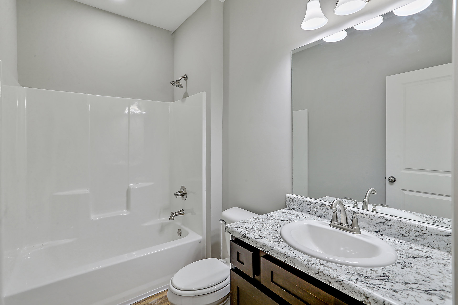 Marble countertop with modern sink and chrome faucet, white toilet with closed lid, glass-enclosed shower, light gray tile walls, and built-in bathtub