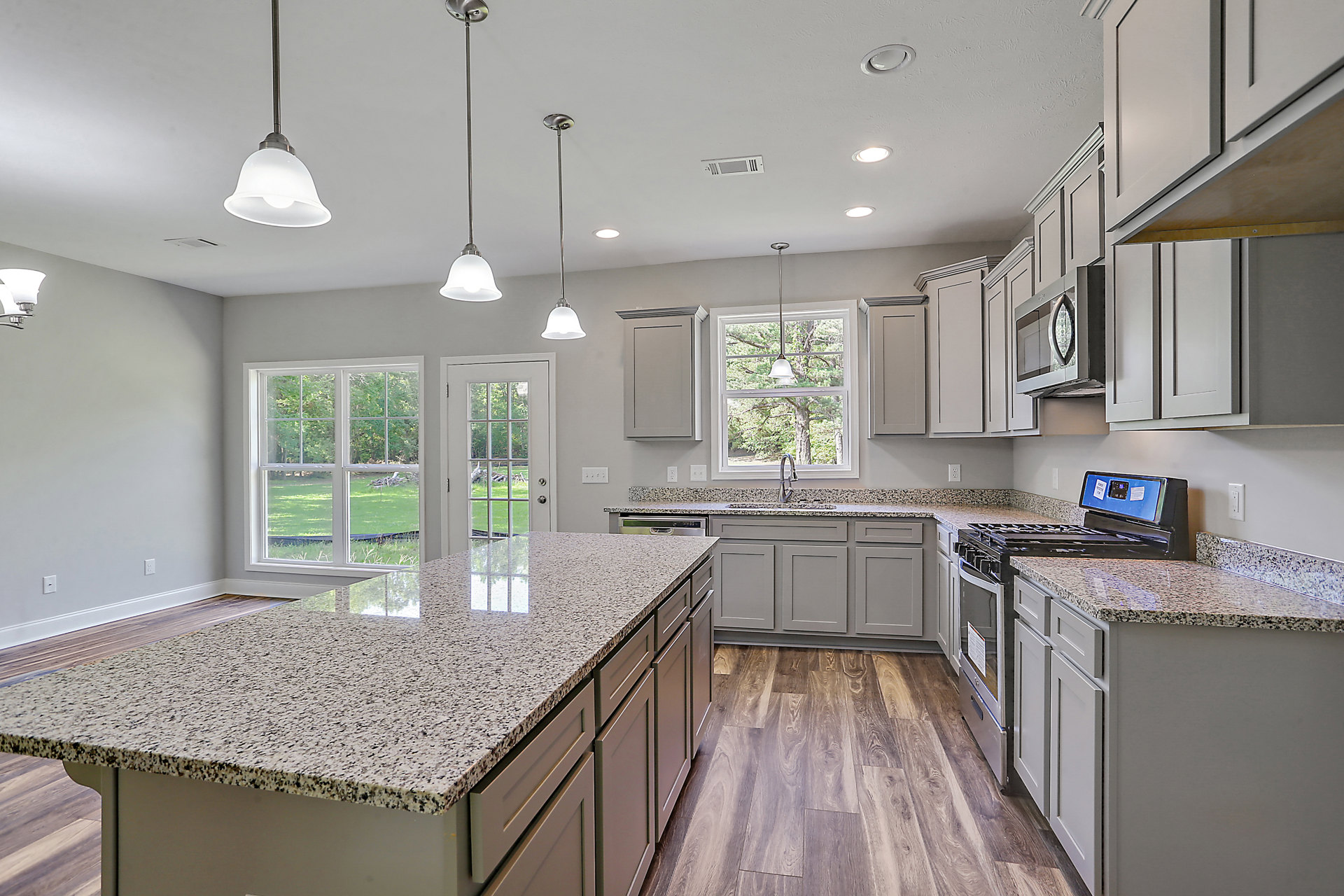 Kitchen with polished granite countertops, wood plank flooring, white cabinetry, stainless steel appliances, and pendant lighting above the island