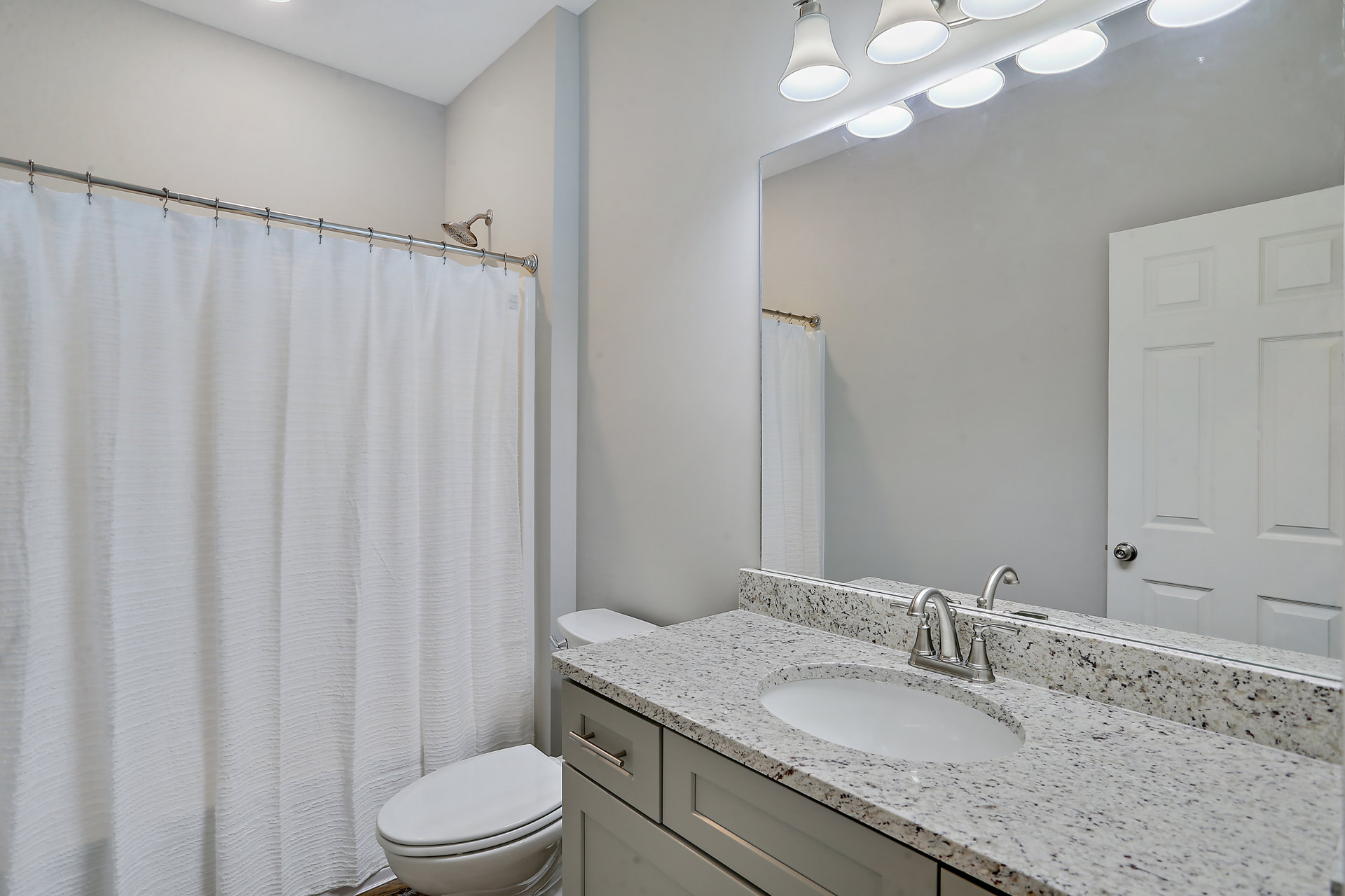 Bathroom with white shower curtain, white toilet, white sink with silver faucet, tiled walls, and white door with cross design