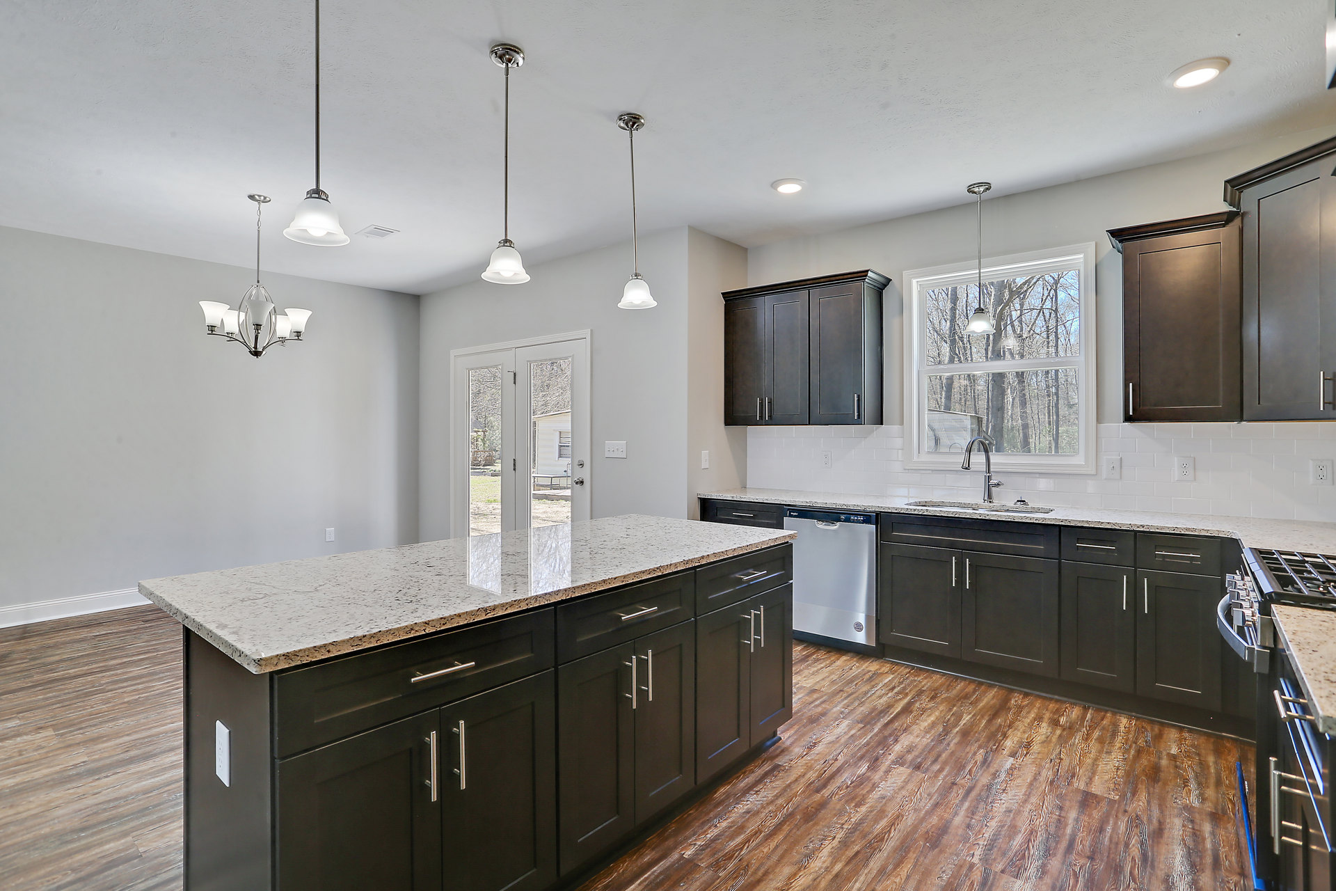 Modern kitchen featuring matte black cabinets with silver handles, white marble countertops, stainless steel sink, pendant light fixture, and large window providing natural light.