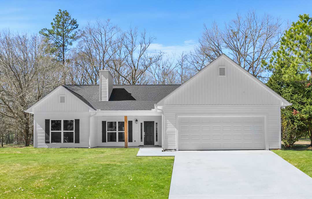 Two-story home with gray siding, black-framed windows, attached garage, manicured lawn, and mature trees in the background