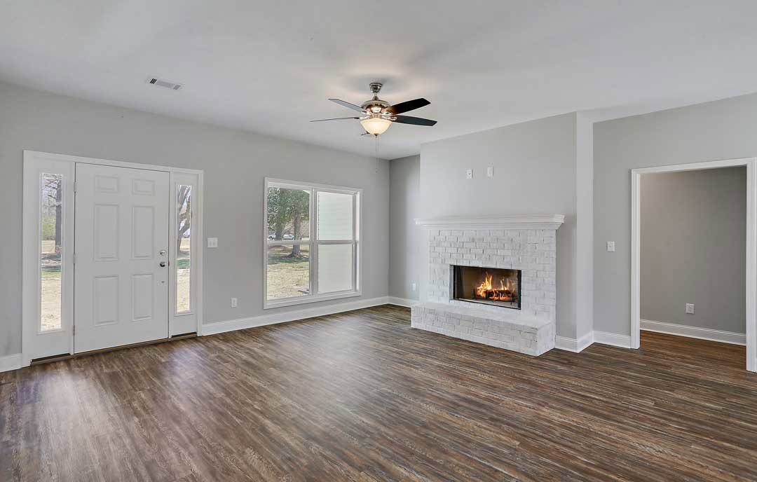 Living room with wood flooring, stone fireplace with active fire, white walls, ceiling fan with light, and white door featuring glass panels.