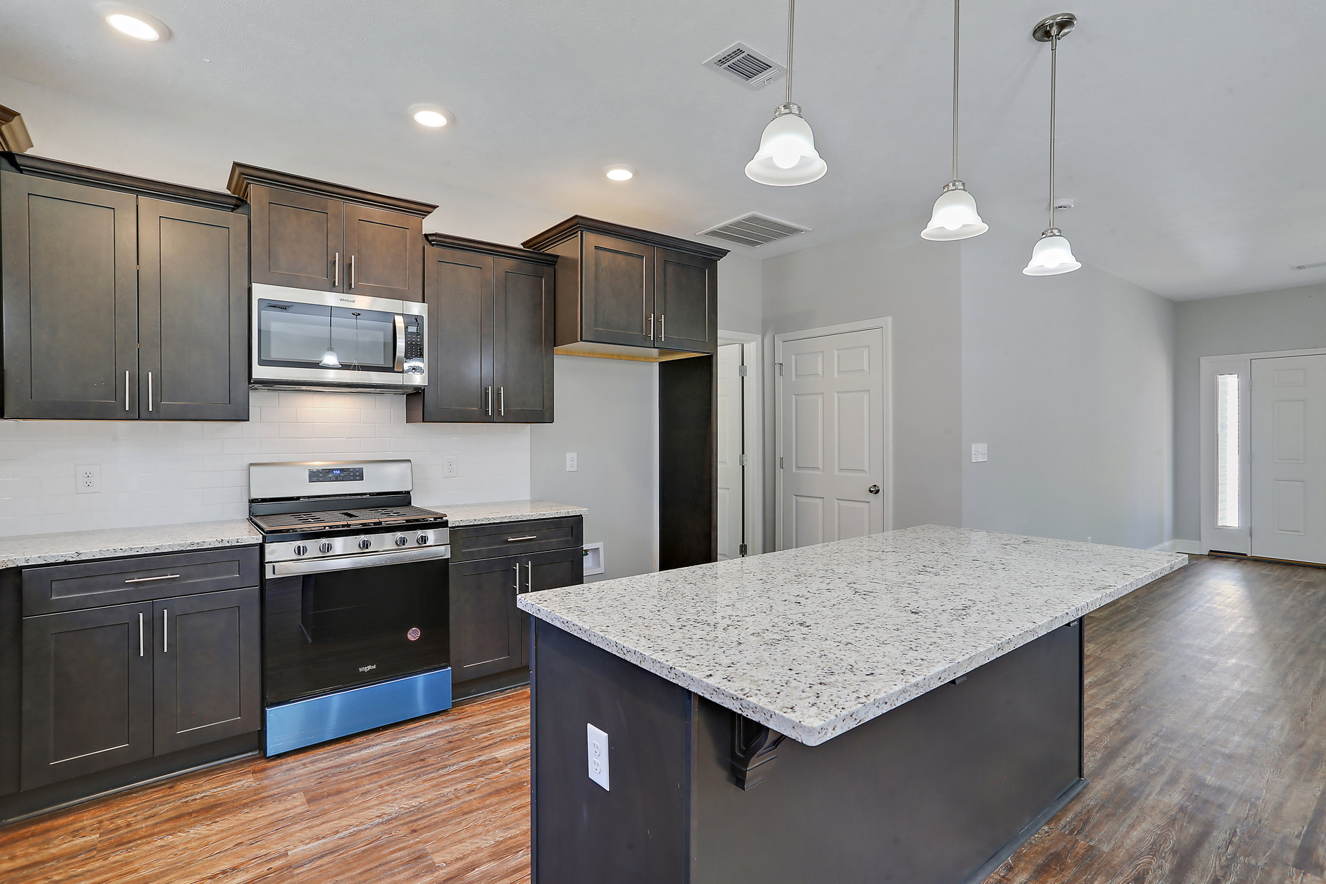 Modern kitchen with white cabinetry, black and white speckled granite countertop, stainless steel stove with glass door, undermount sink, pendant ceiling light, and light wood