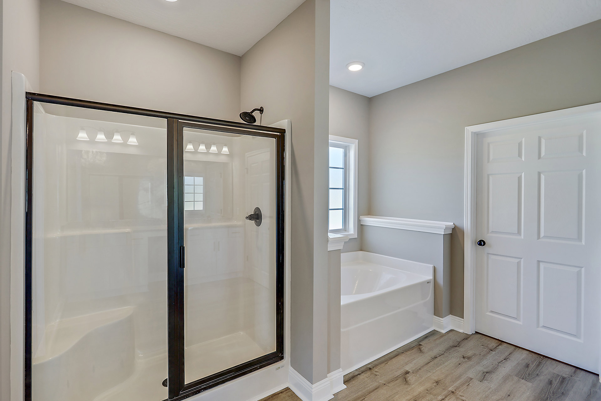 Bathroom featuring a frameless glass shower enclosure, built-in bathtub with tile surround, white paneled door with round metal knob, chrome shower head, and window providing