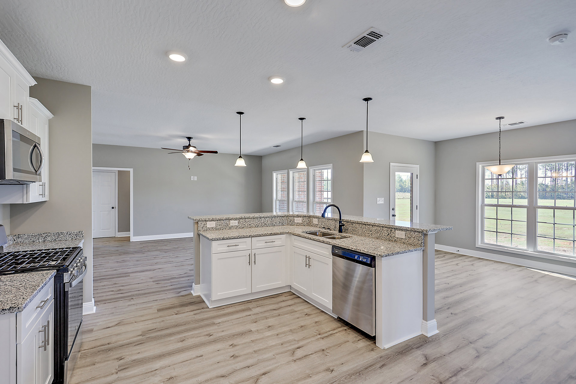 Spacious kitchen featuring a marble island with a black faucet, white cabinetry, stainless steel stove and oven, ceiling fan with light fixture, large window letting in natural