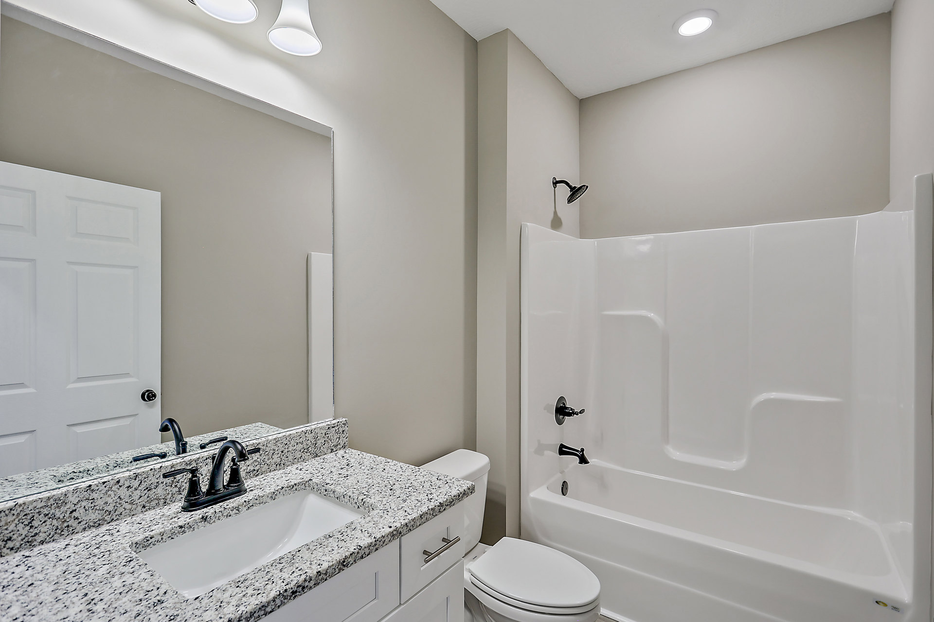 Marble countertop with black faucet, rectangular sink, glass-enclosed shower, white bathtub, and toilet against light tile walls