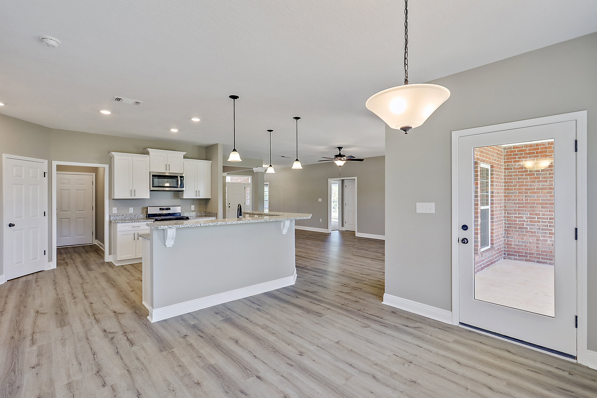 Open-concept kitchen and living room featuring granite countertops, white cabinetry, laminate flooring, plaster walls, ceiling light fixture, and two white doors with silver