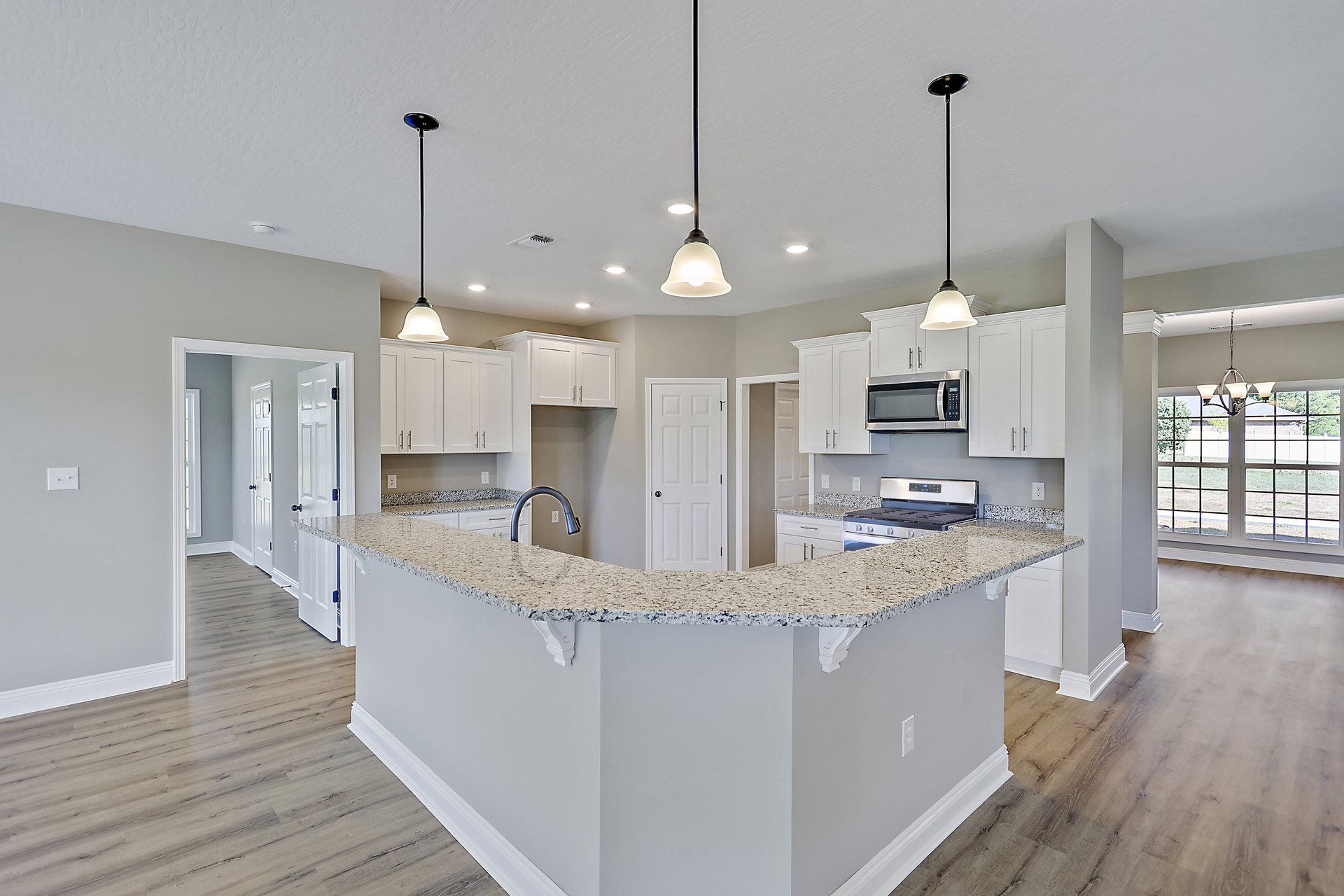 Marble countertop kitchen with white cabinetry, stainless steel microwave, black hardware, and light flooring