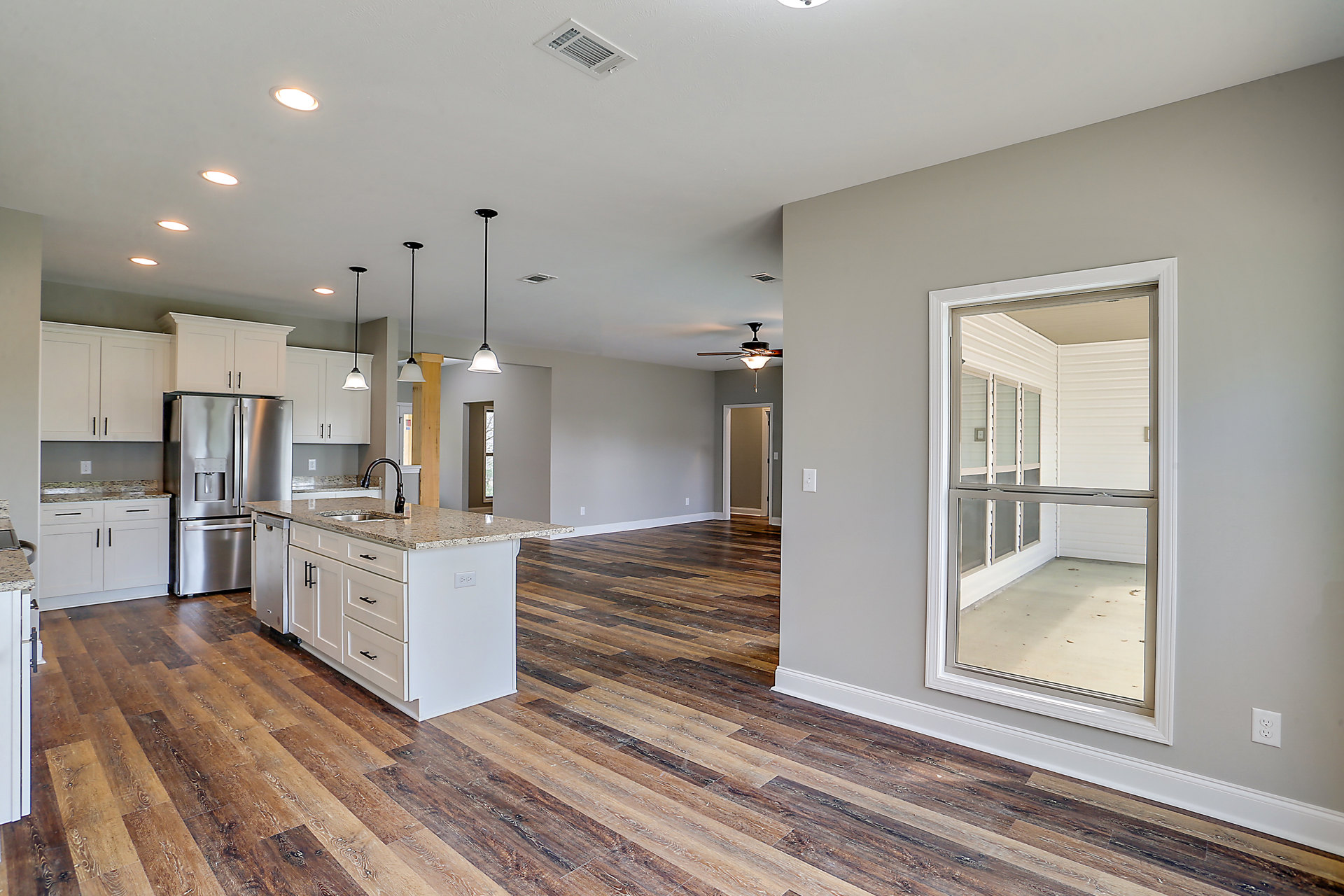 Open kitchen and living room featuring hardwood flooring, stainless steel refrigerator, white cabinets with marble countertops, large window, white kitchen island with marble