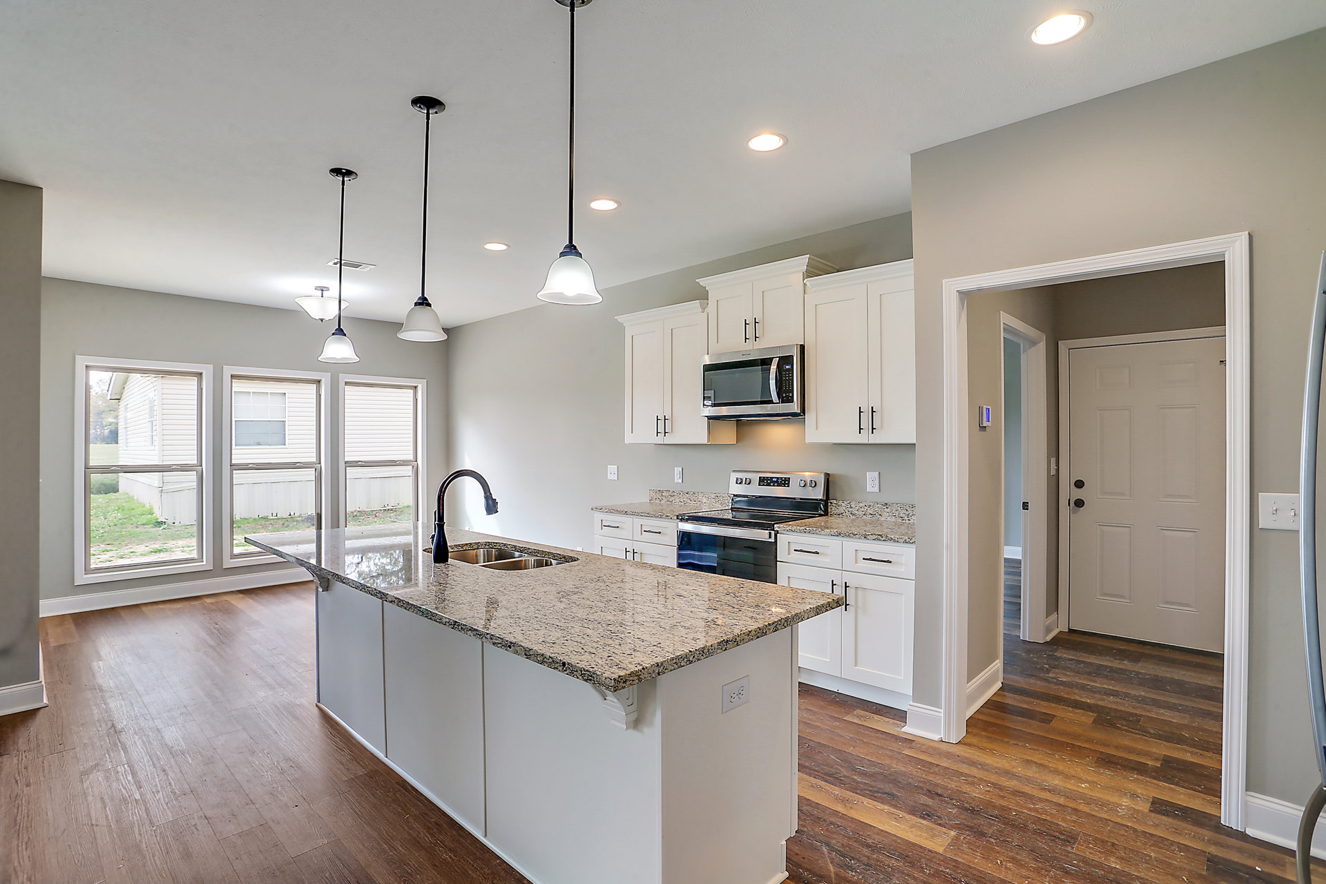 Granite kitchen island with built-in sink and black soap dispenser, wood flooring, stainless steel stove and microwave, white cabinetry with black knobs, recessed ceiling light