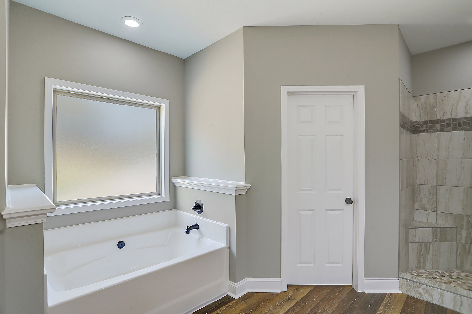 Bathroom with white bathtub and silver faucet, frosted glass window, white door with round knob, tiled shower stall with built-in shelf, and white shelf beneath window
