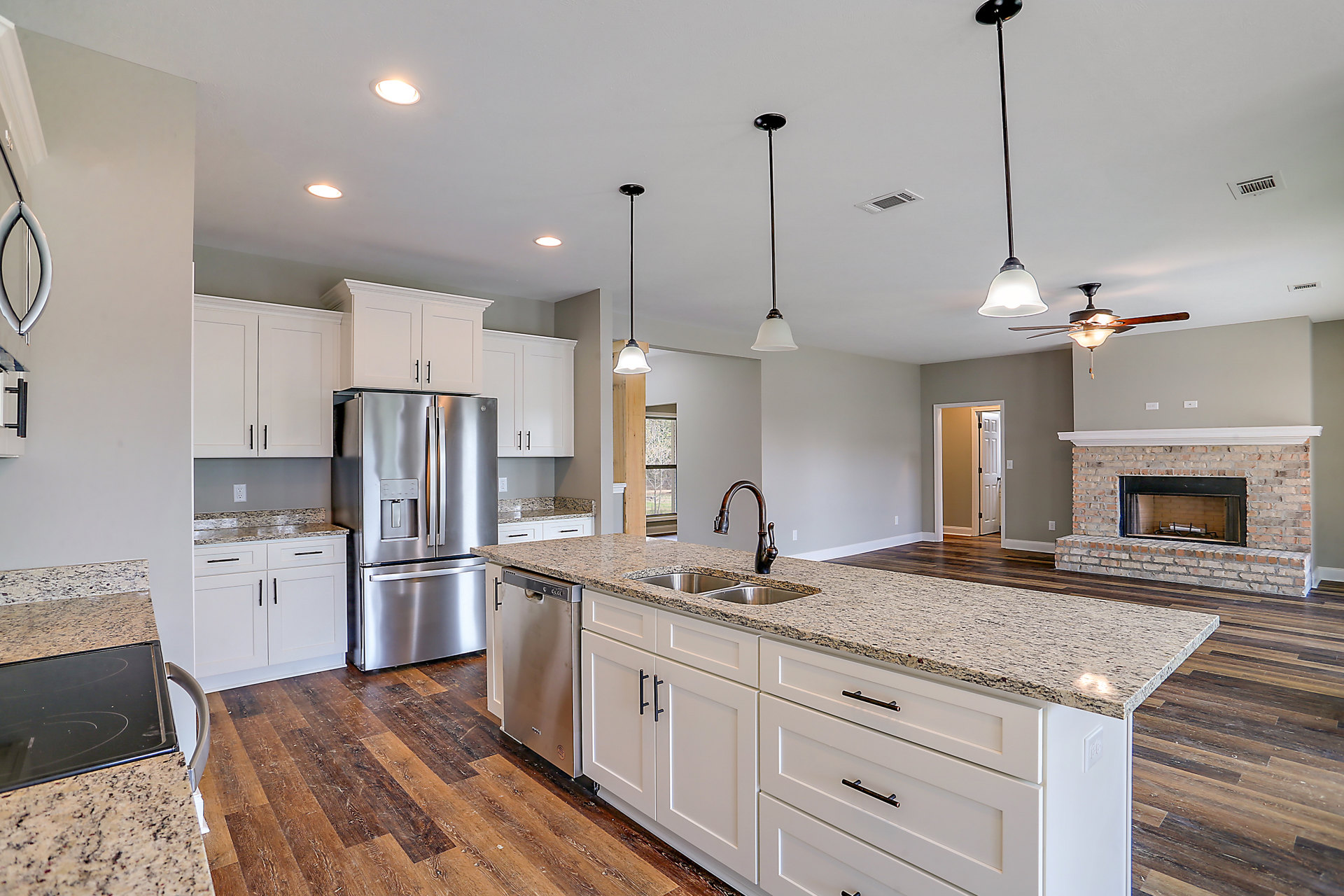 Spacious kitchen featuring a large quartz island with built-in sink, stainless steel refrigerator and oven, white cabinetry, pendant lighting, and hardwood flooring