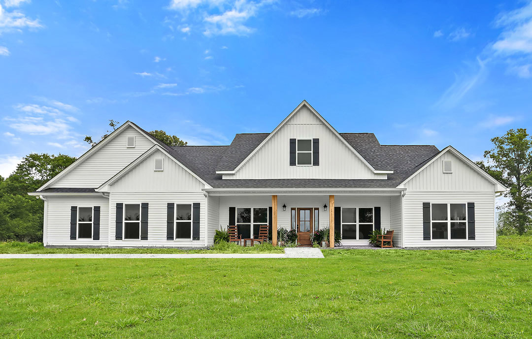 White house with black roof, white-framed windows with black shutters, front porch, green lawn, Robert Frost Farm visible in the background under partly cloudy sky
