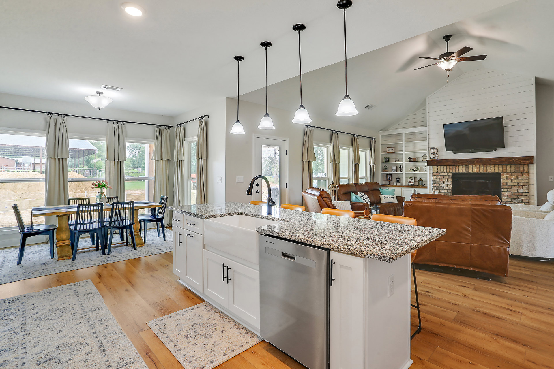 Open-concept kitchen and living room featuring a large central island with stone countertop, modern cabinetry, stainless steel appliances, wood flooring, and seating area near