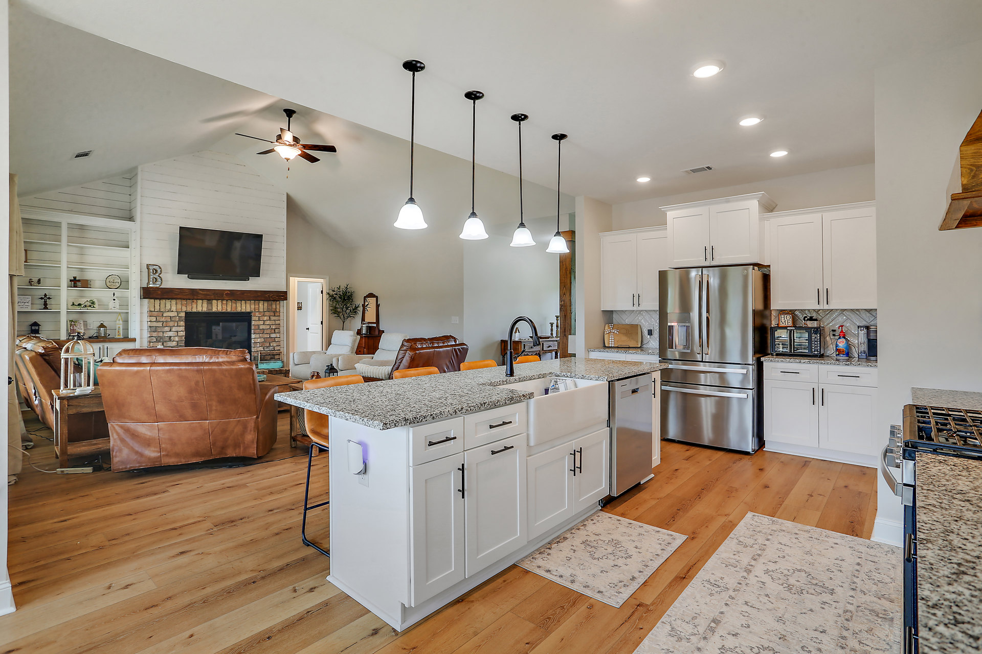 Spacious kitchen featuring a large central island with stone countertop, stainless steel refrigerator, white cabinetry, wood flooring, and modern lighting fixtures