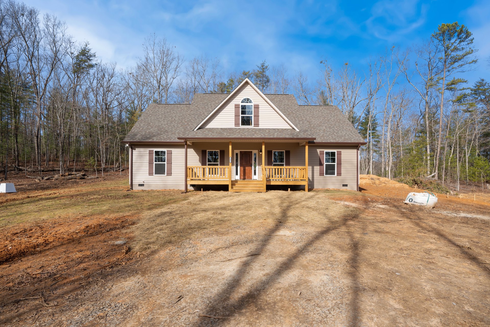 Two-story house with wood porch, white-framed windows, wooden steps, and a dirt driveway; dirt yard features a deck and a large white bag with black text.