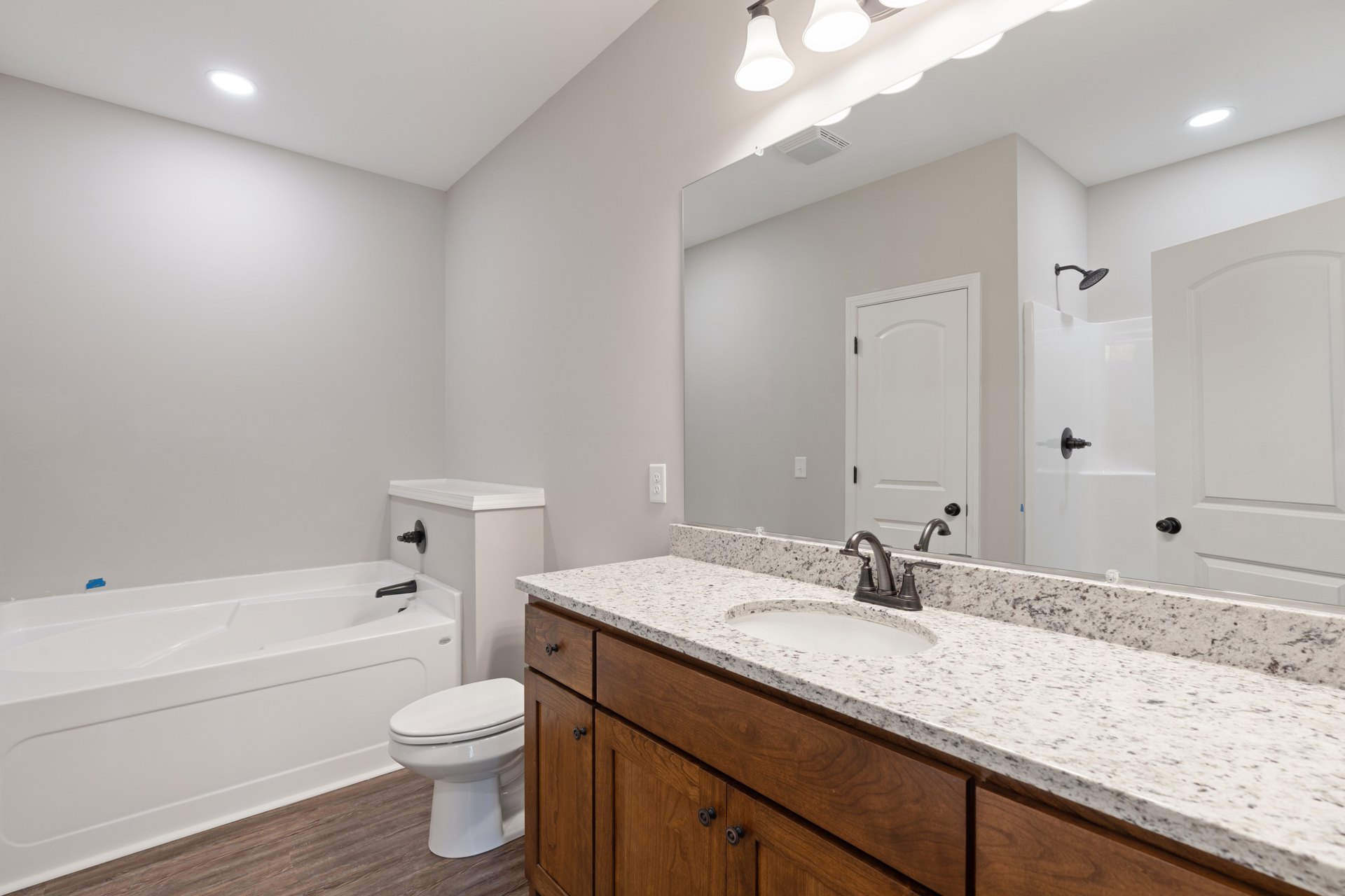 Bathroom with white tile floor, white toilet, built-in bathtub, white sink set in light cabinetry, black hardware on white door, chrome faucet, and neutral wall paint.