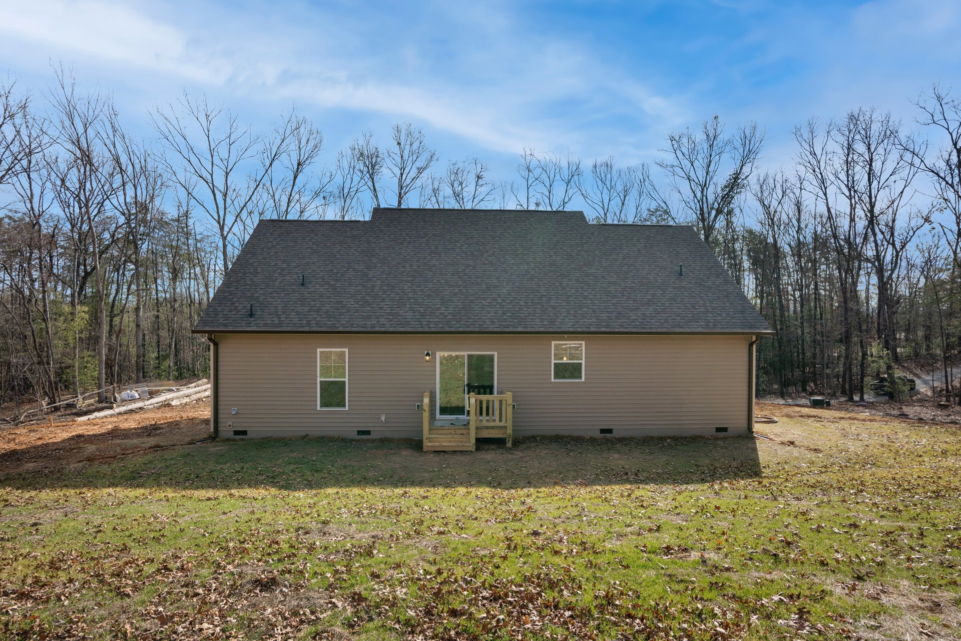 Two-story house with white-framed windows, covered porch with wooden bench, front stairs leading to entry door, green lawn and mature trees in background, gray shingle roof under