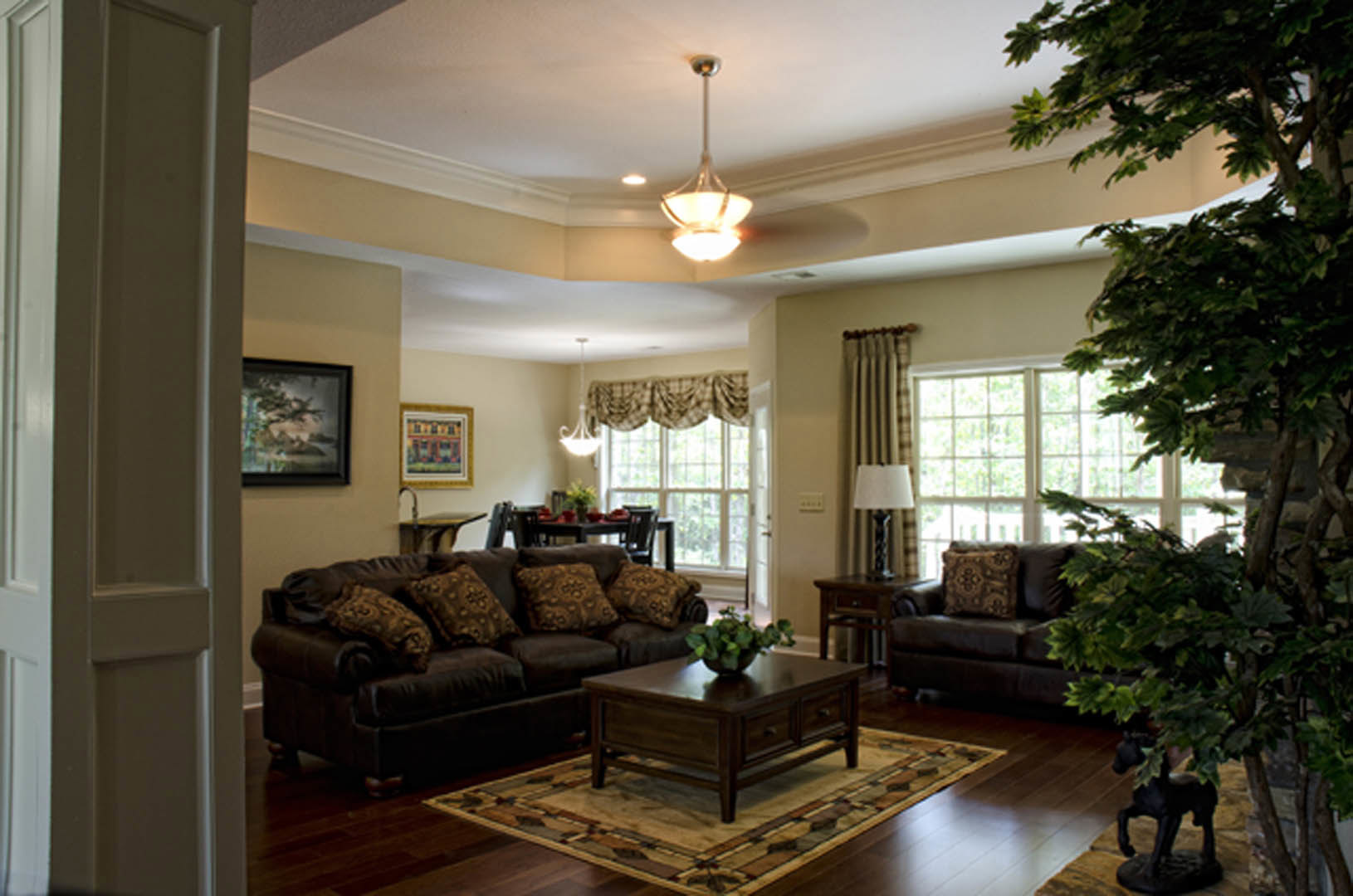 Spacious living room with light-colored couches, decorative pillows, large indoor tree, wood coffee table, neutral walls, and soft natural lighting