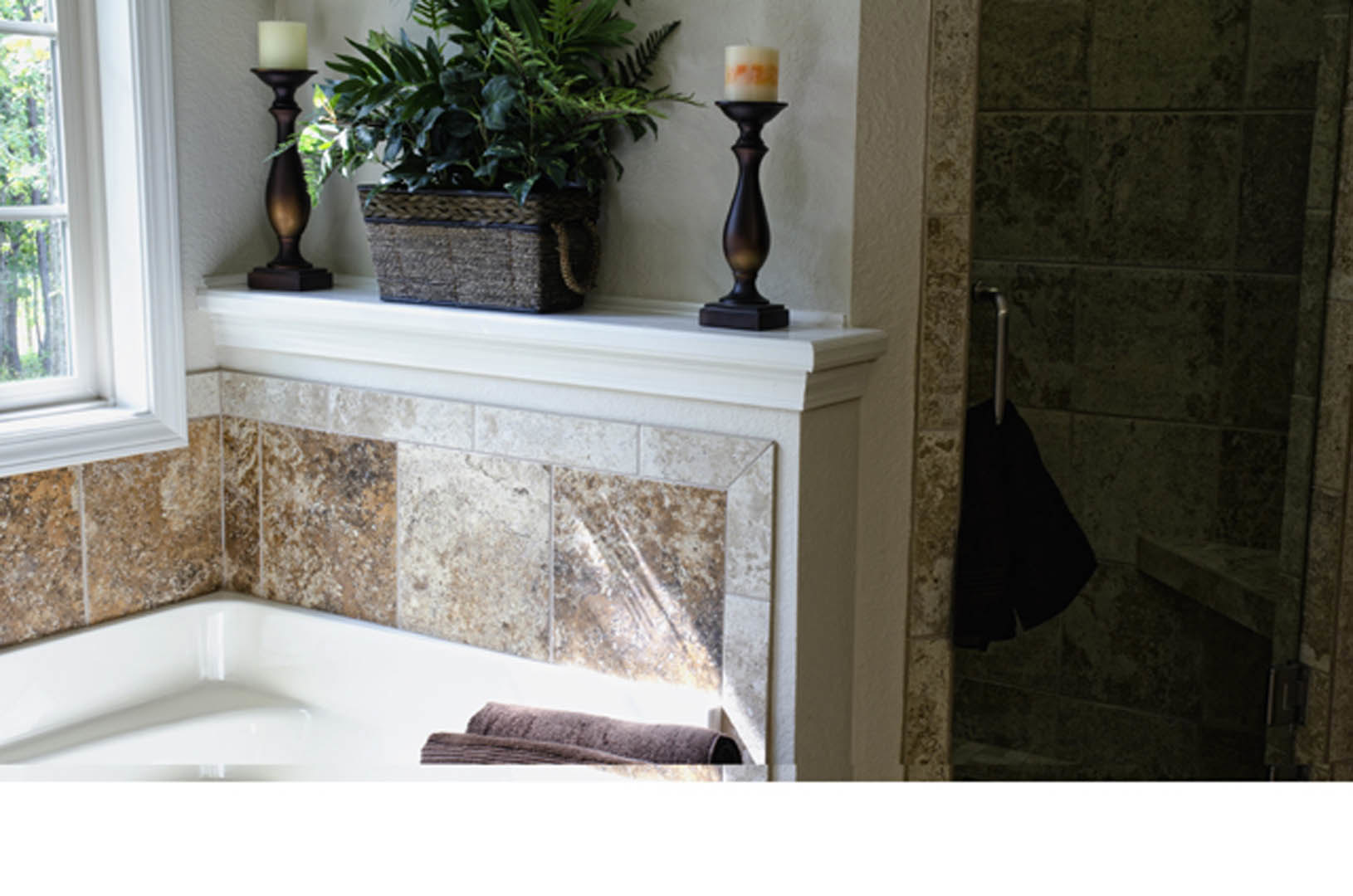 Freestanding bathtub surrounded by lit candles and potted plants, woven basket planter, blurred vase on nearby surface, neutral bathroom finishes