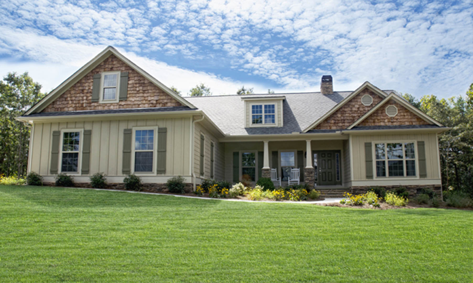 Two-story home with white siding, covered front porch, manicured lawn, flower beds, and Robert Frost Farm visible in the background under a partly cloudy sky
