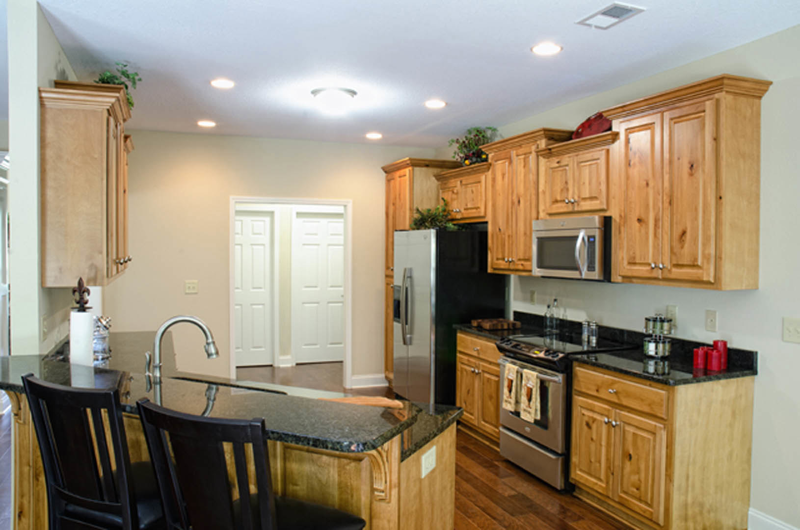 Kitchen featuring black countertop, wooden cabinets, stainless steel refrigerator, built-in microwave, stove and oven, sink, and a white door reflected in a mirror