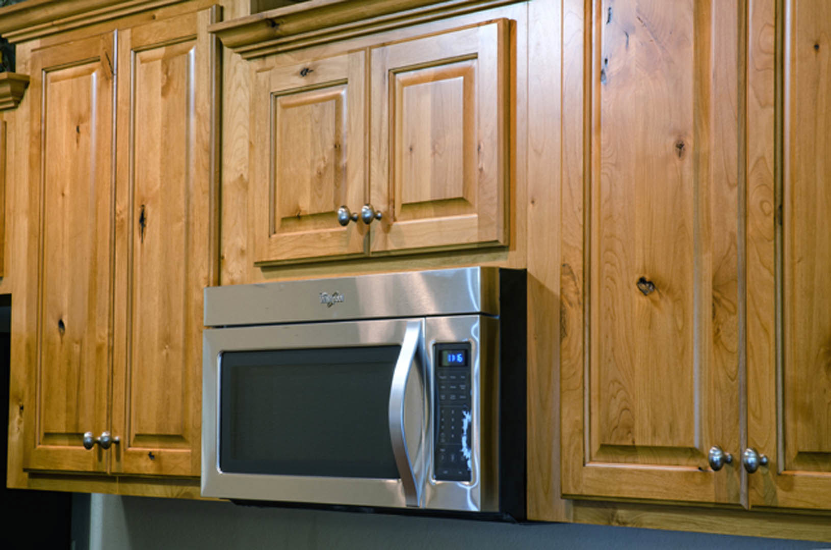 Microwave oven installed above light wood cabinetry with silver handle, set against a neutral kitchen wall