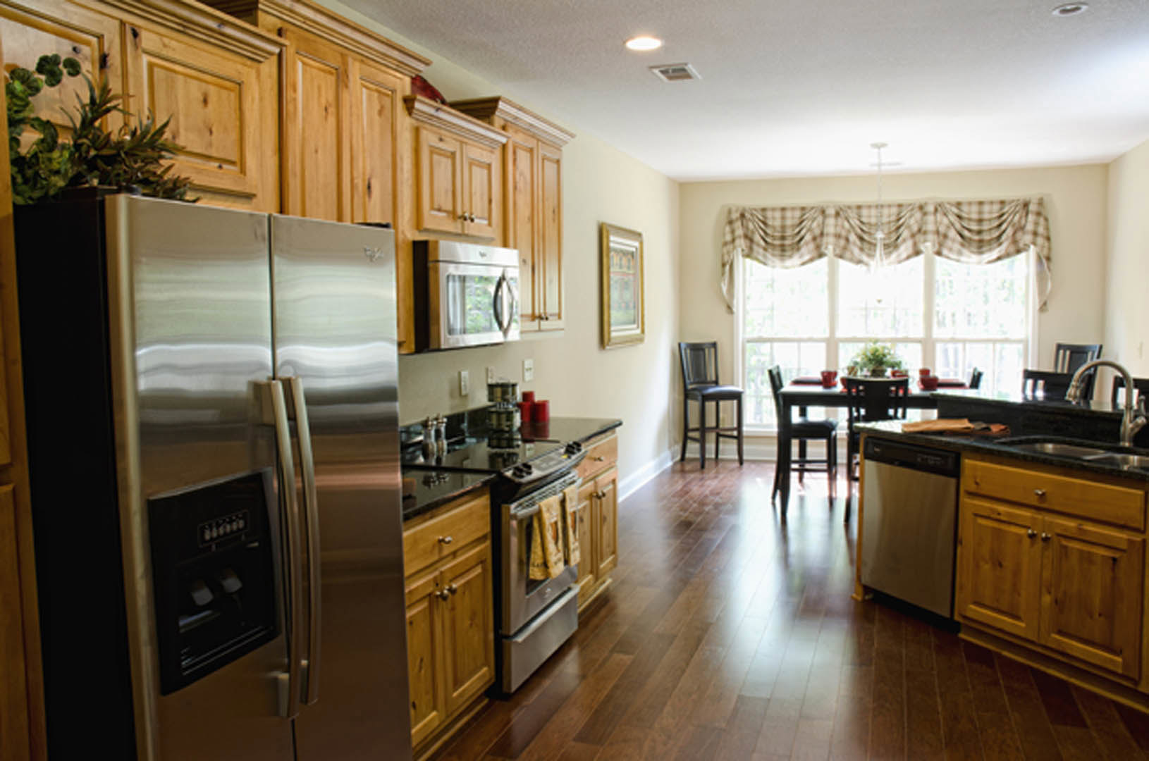 Kitchen with natural wood cabinets, stainless steel refrigerator with ice and water dispenser, black chair against wall, built-in microwave with glass door, stove and oven, light