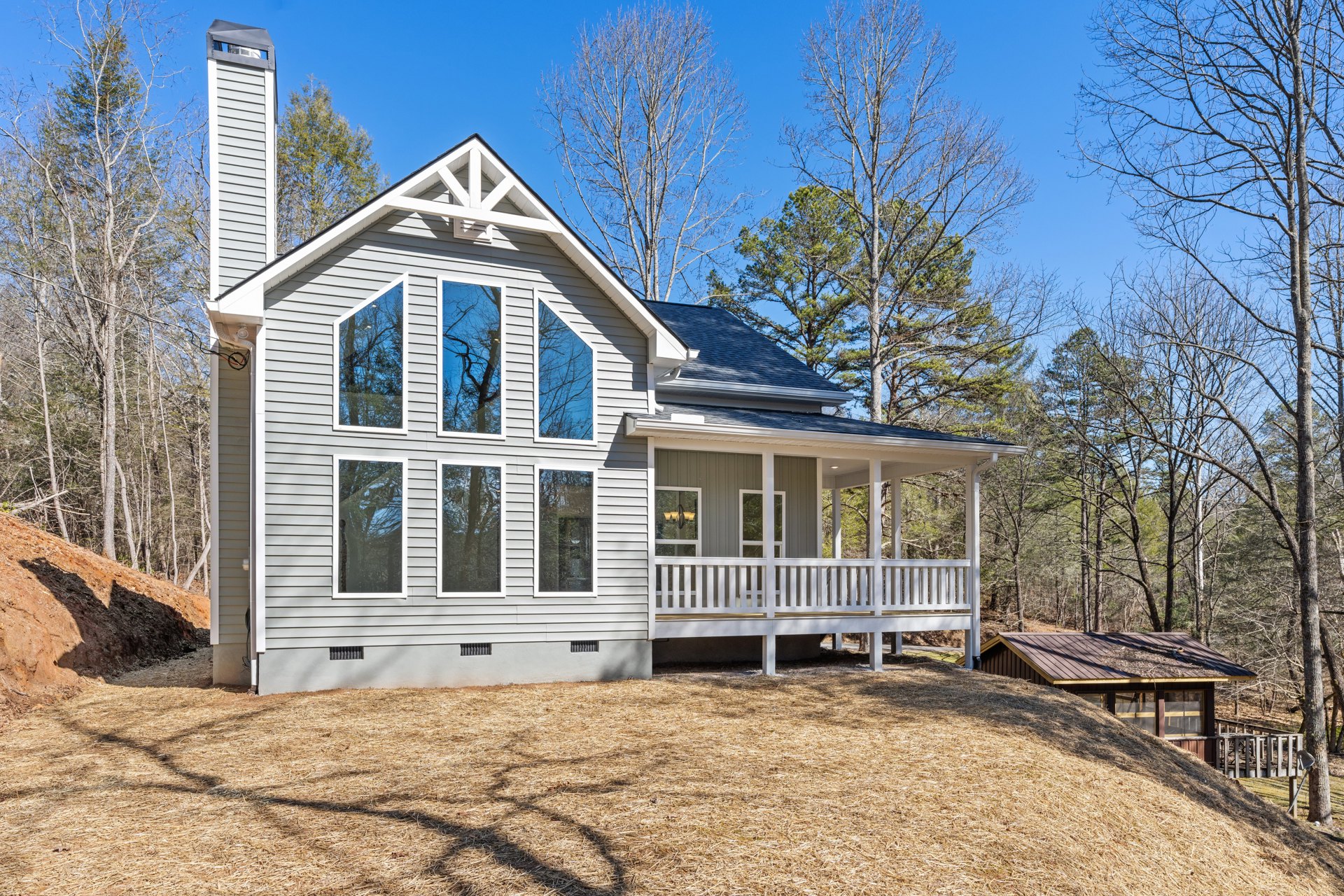 Two-story home with white porch railing, spacious deck, multiple large windows reflecting blue sky and nearby trees